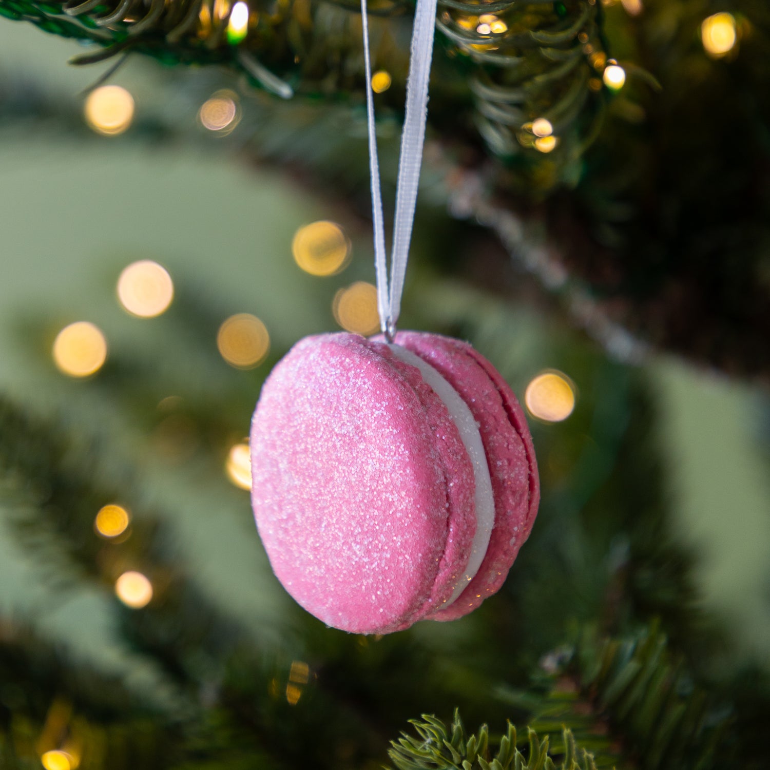 Pink macaron ornament hanging on a Christmas tree with blurred lights in the background.