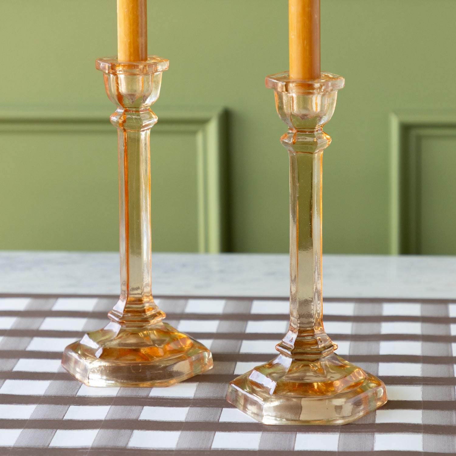 Two amber-colored candles in Amber Glass Candle Holders on the Brown Painted Check Runner.
