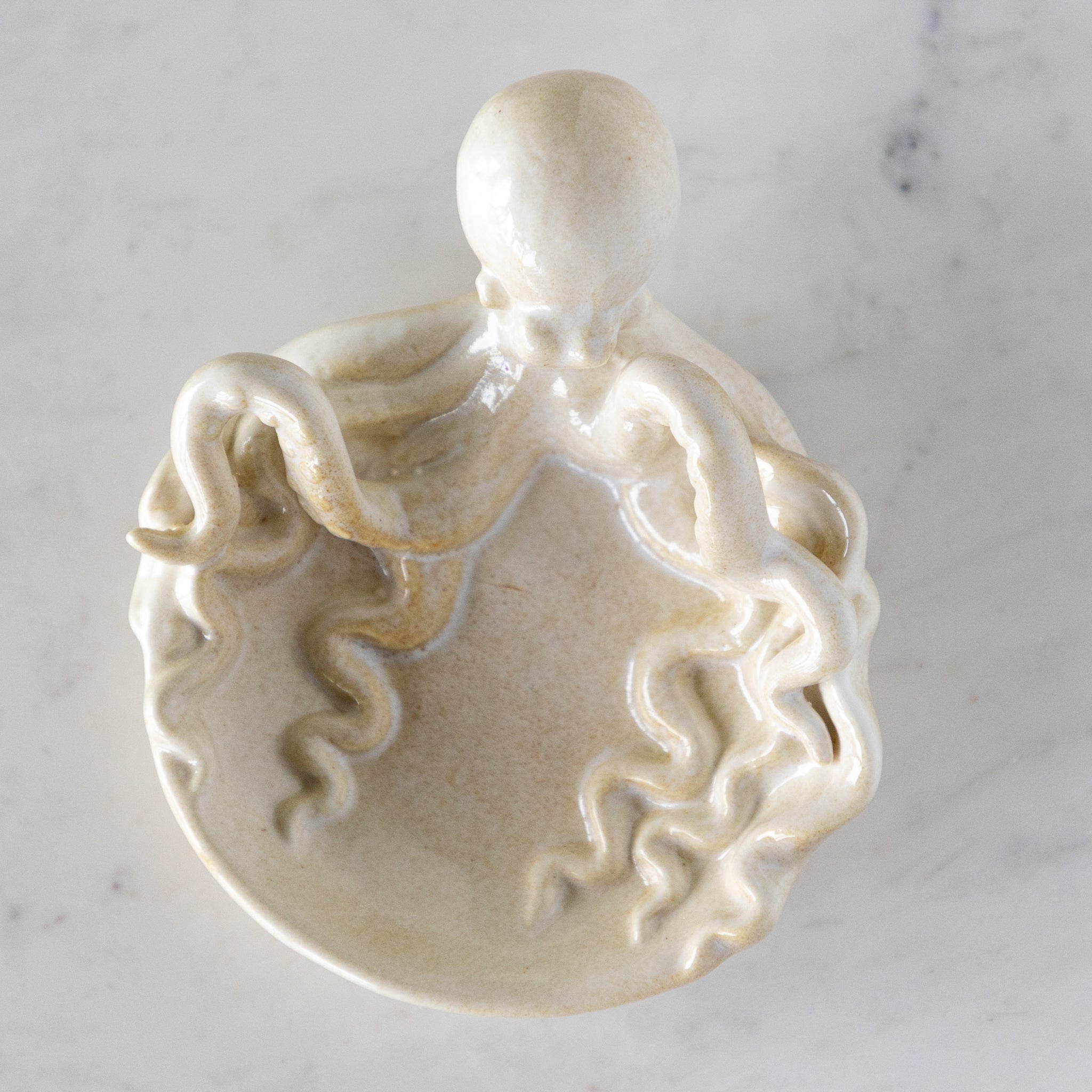 A Stoneware Octopus Dish featuring an octopus with its tentacles around a circular dish, on a marble table.