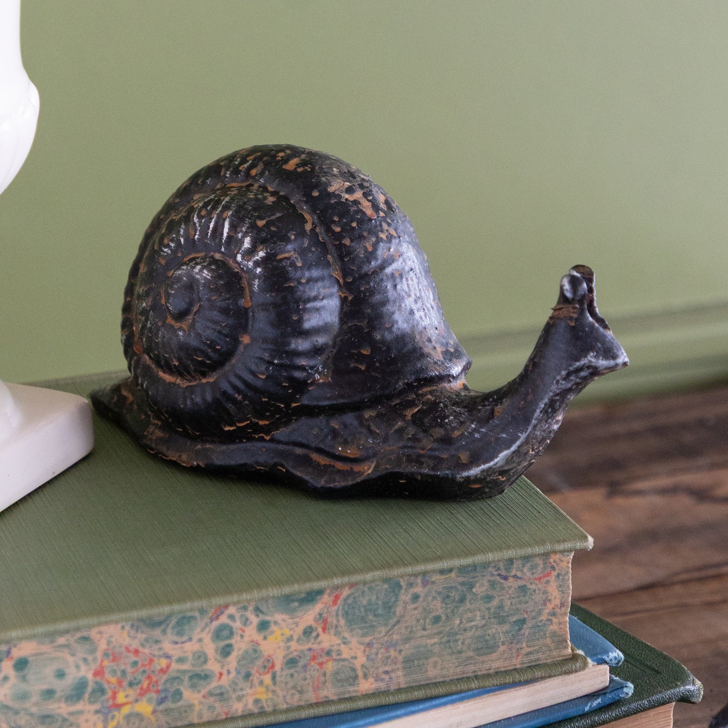 Decorative metal snail on top of a stack of books with a green background.