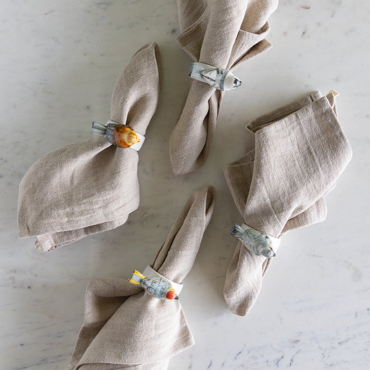 Stoneware Napkin Rings w/ Perched Bird around beige napkins.
