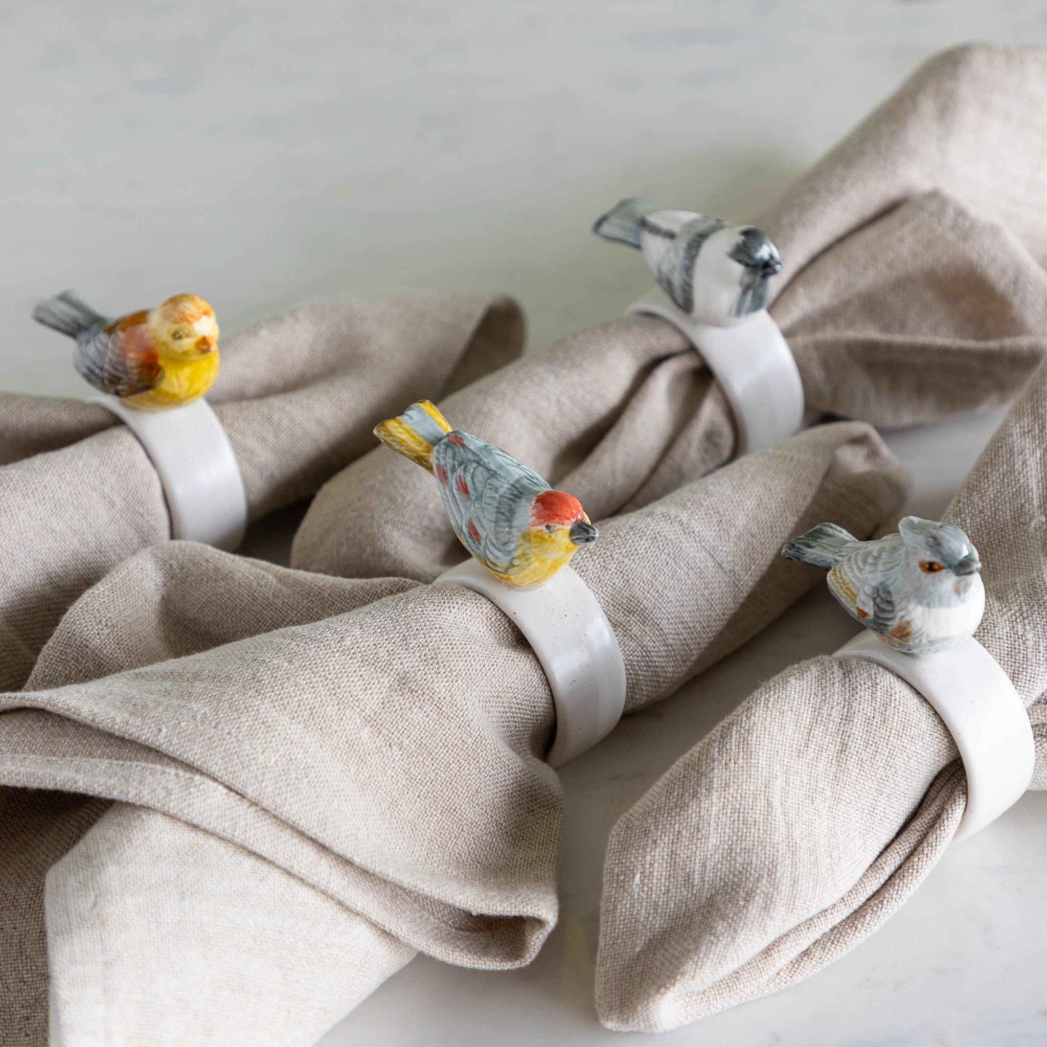 Stoneware Napkin Rings w/ Perched Bird around beige napkins.