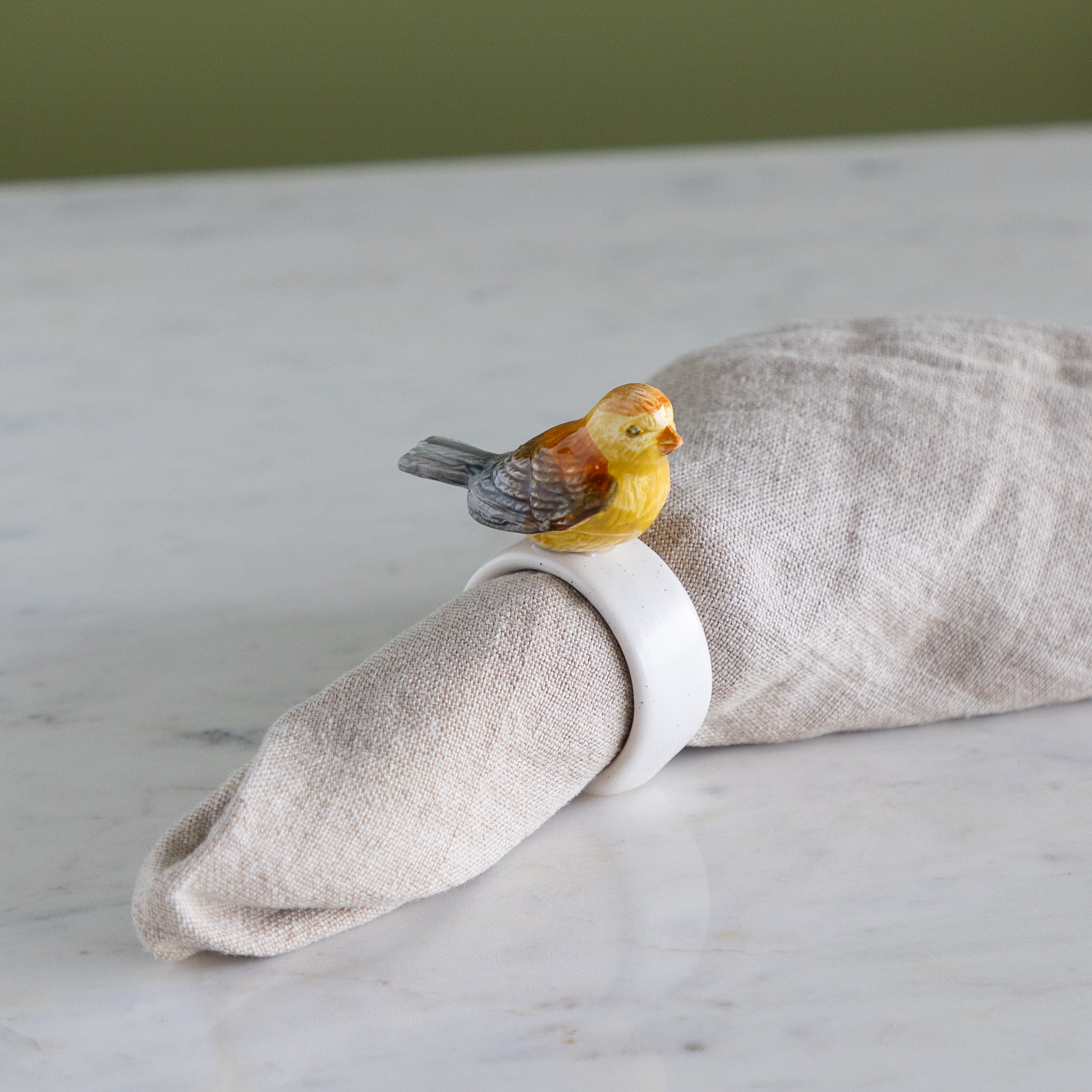 Napkin ring with colorful bird design around a folded beige napkin against a neutral background.