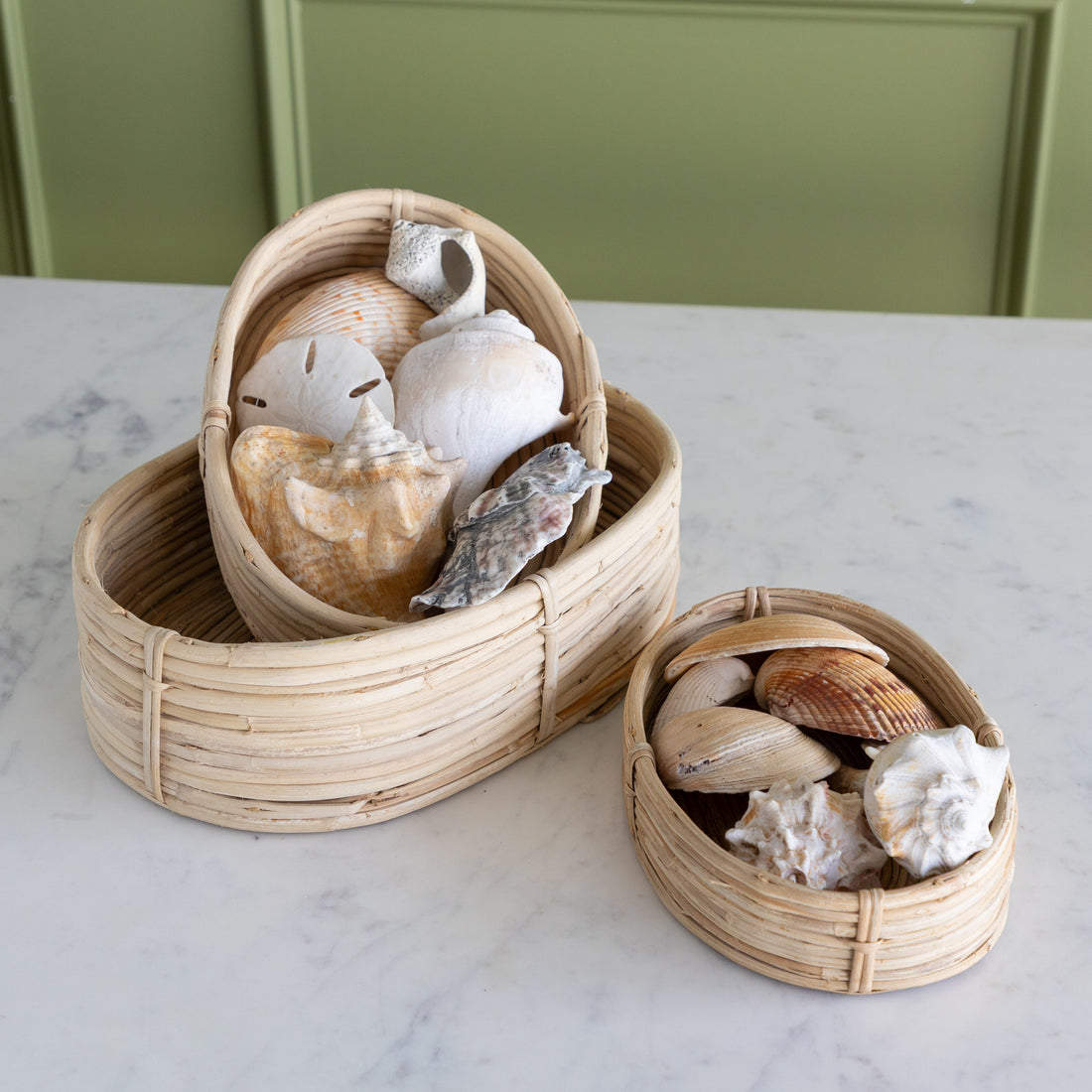 Three woven baskets with seashells on a marble surface