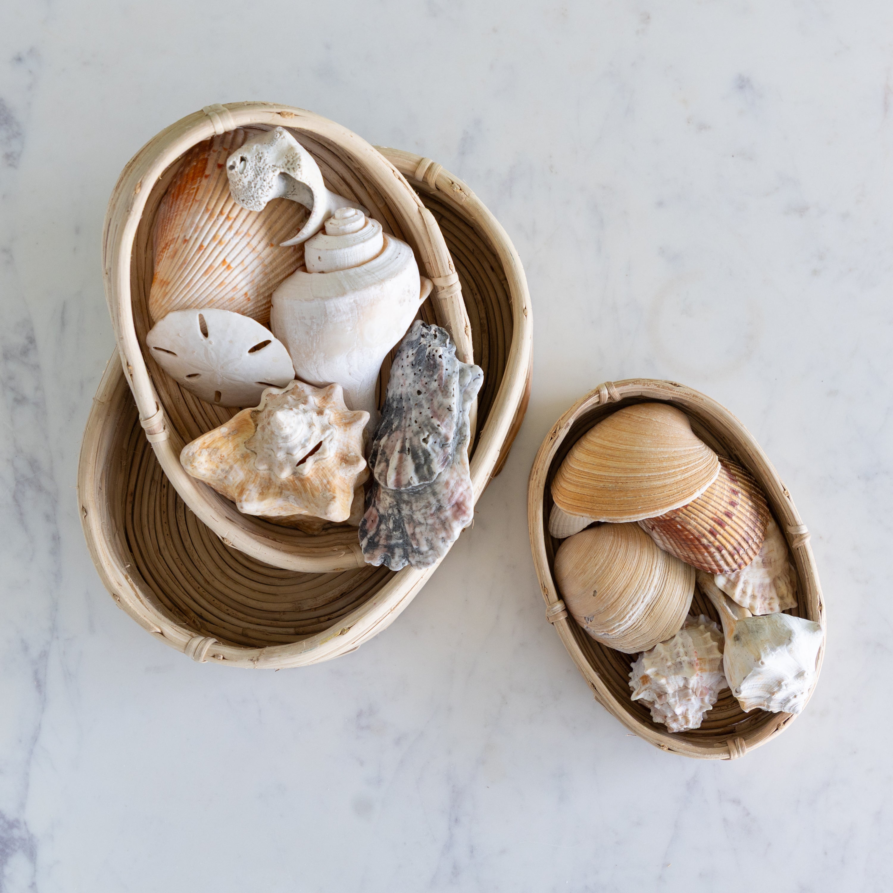 Two woven baskets filled with seashells on a marble surface