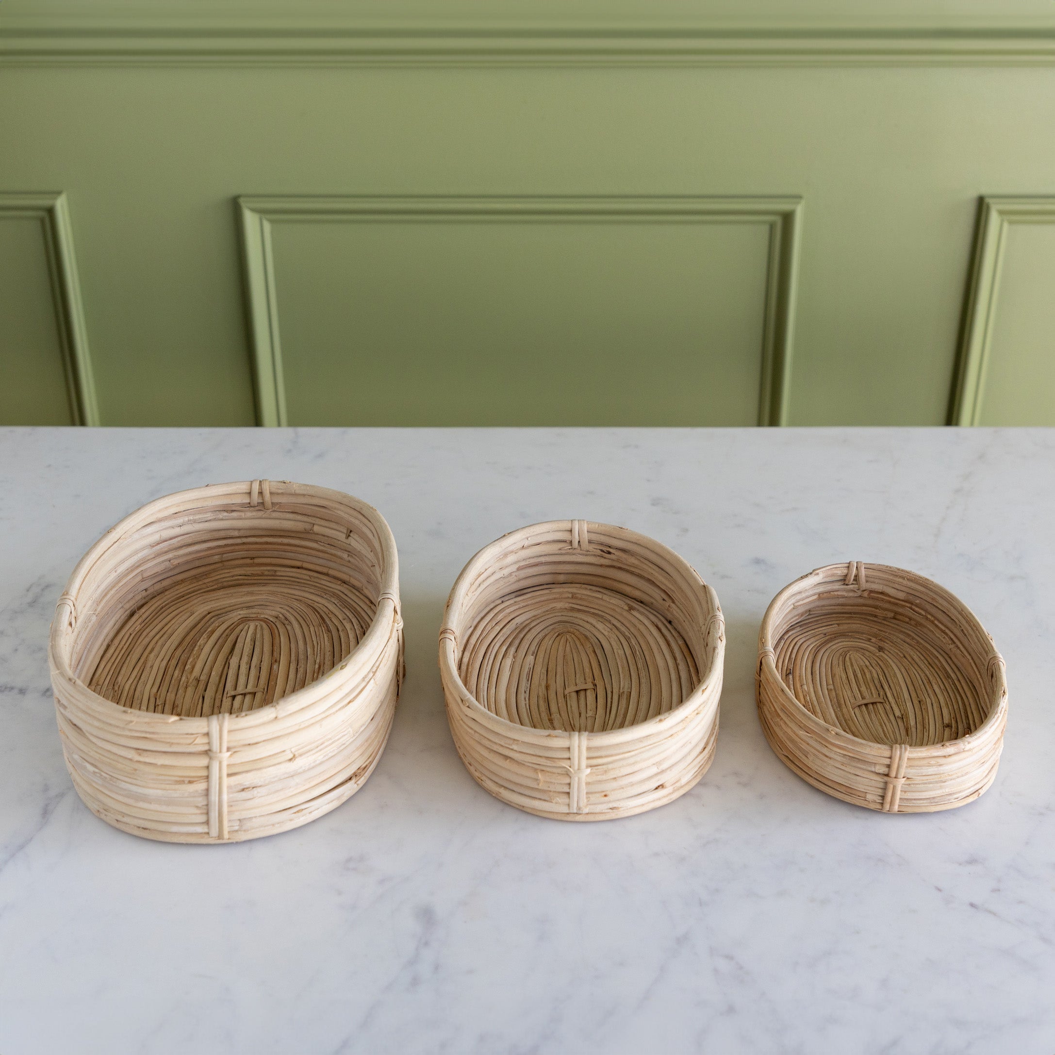 Three woven baskets of different sizes on a marble surface with a green paneled wall in the background.
