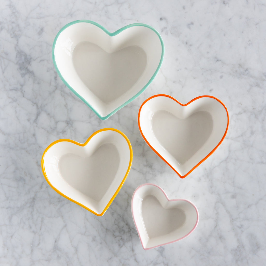 Four heart-shaped bowls with colorful rims on a marble surface.