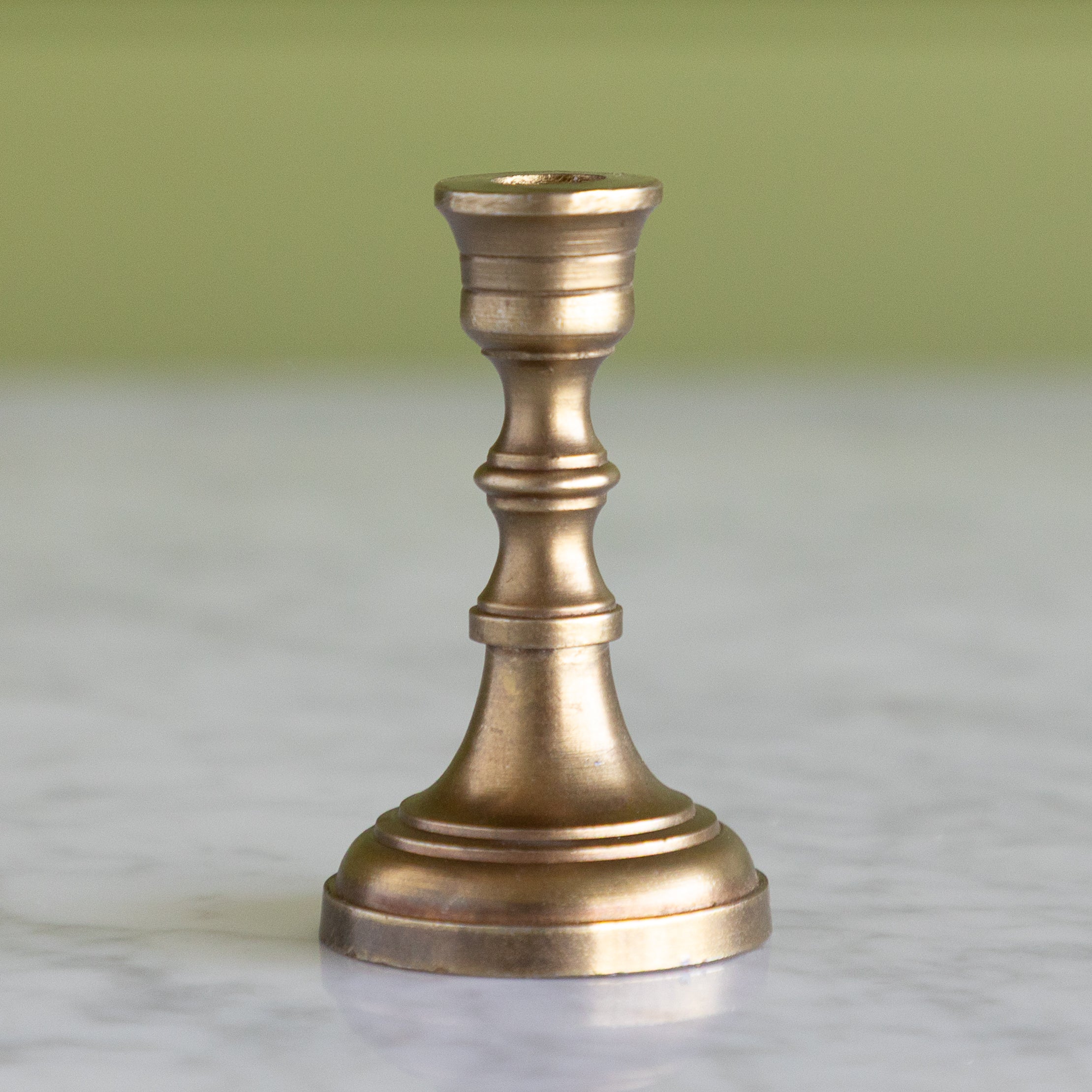 Bronze candlestick on a marble surface with a green background.