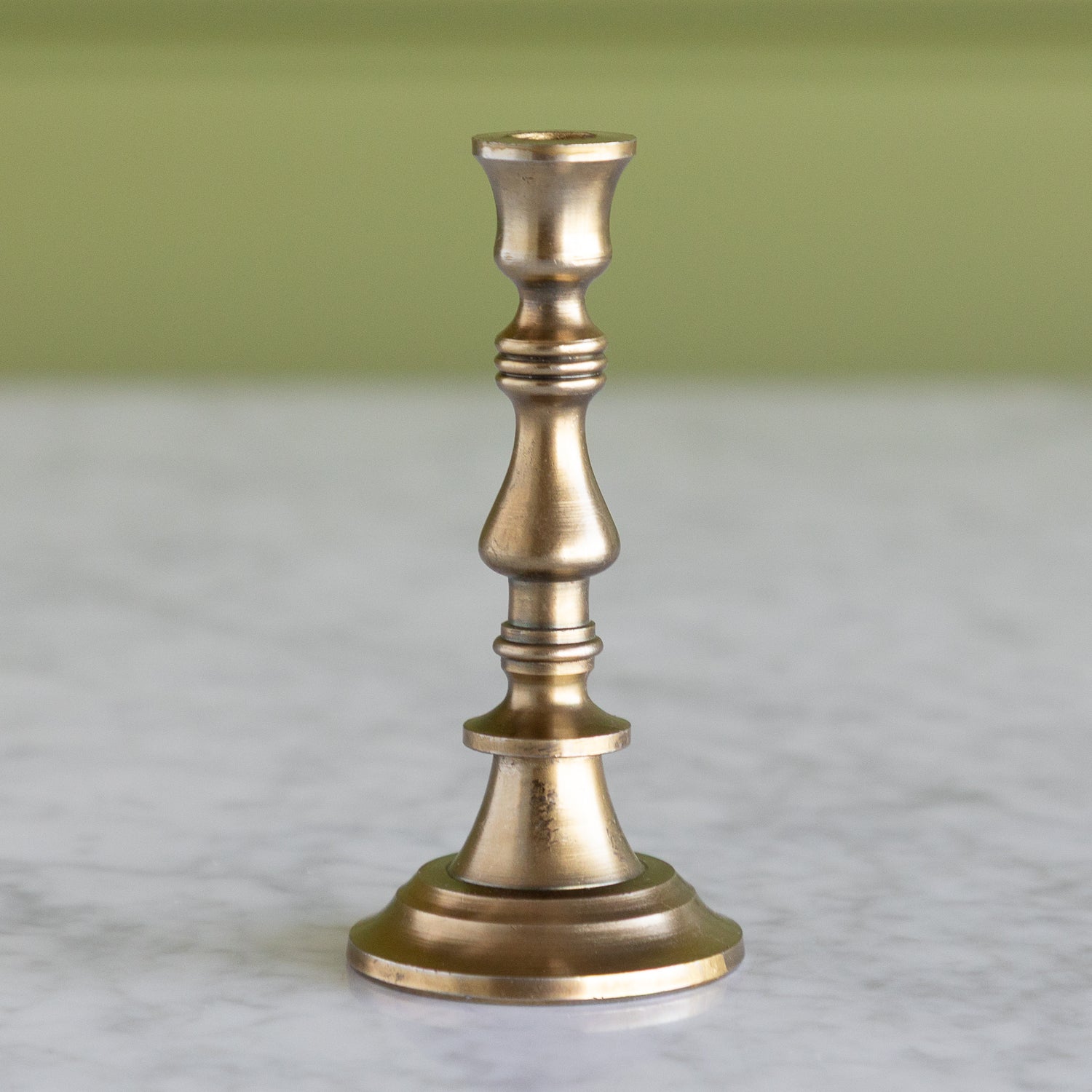 Brass candlestick on a marble surface with a green background.