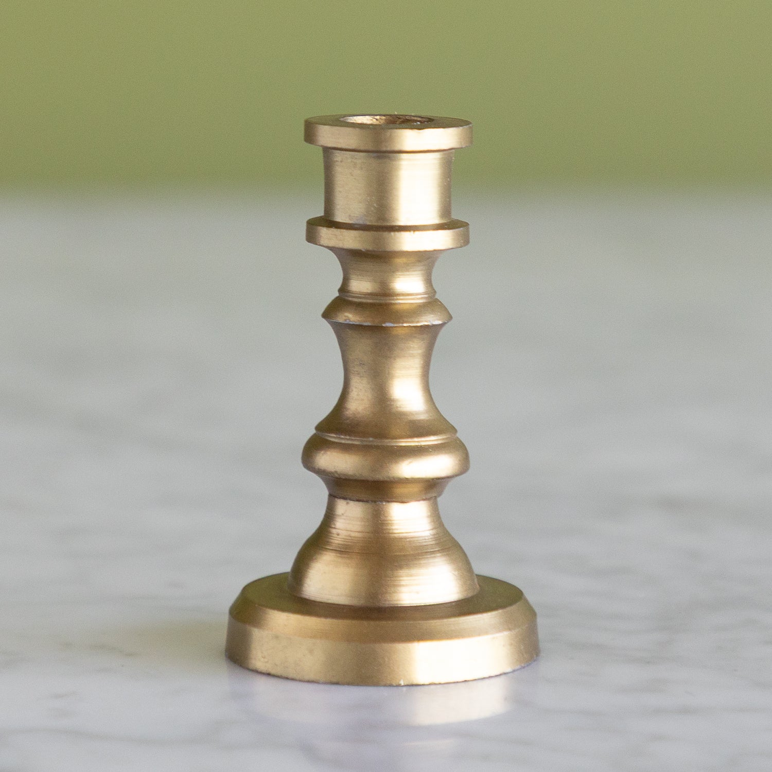 Brass candlestick on a marble surface with a green background.