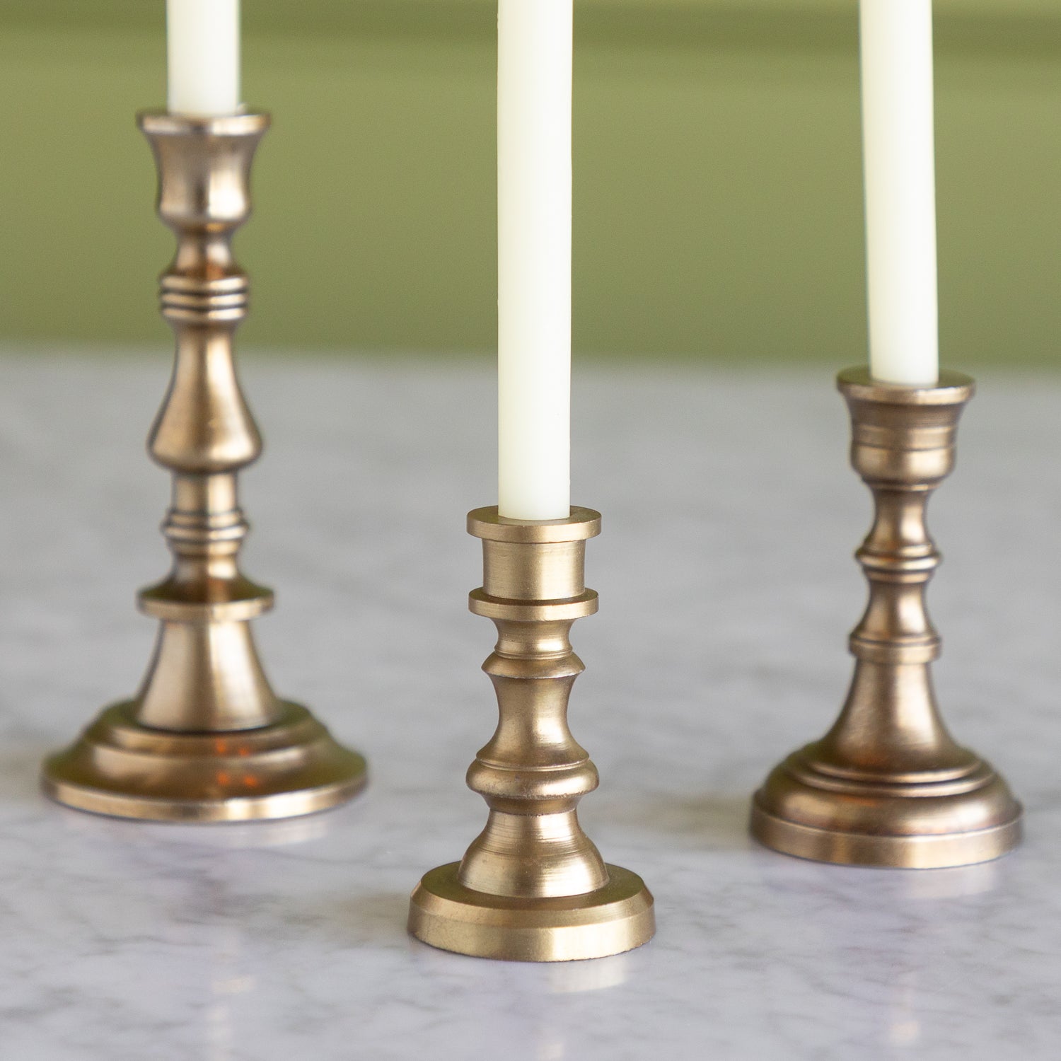 Three brass candle holders with white candles on a marble surface.