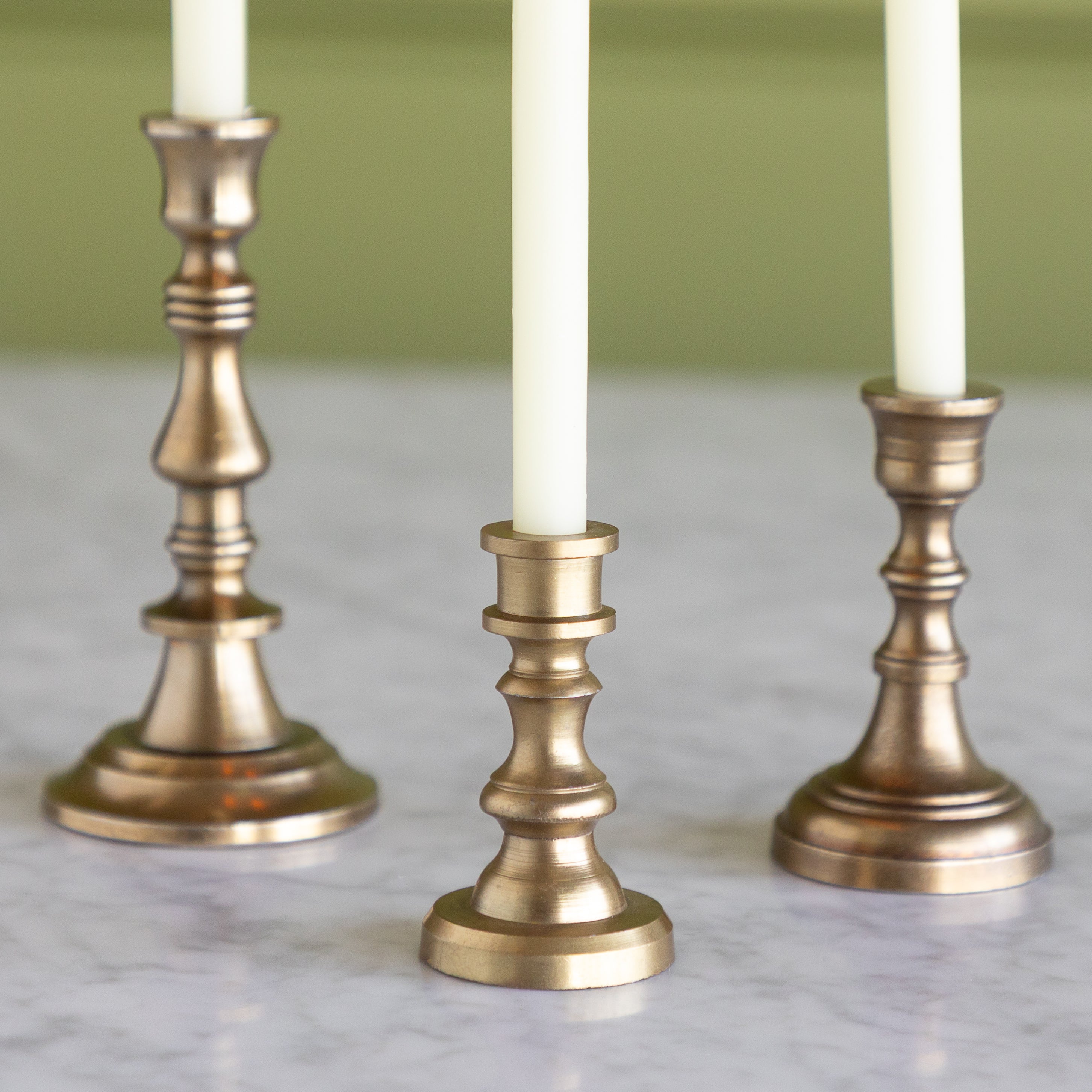 Three brass candle holders with white candles on a marble surface.