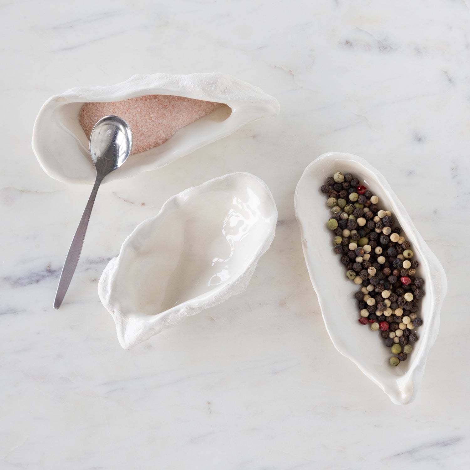 White ceramic oyster-shaped bowls with a spoon on a marble surface.