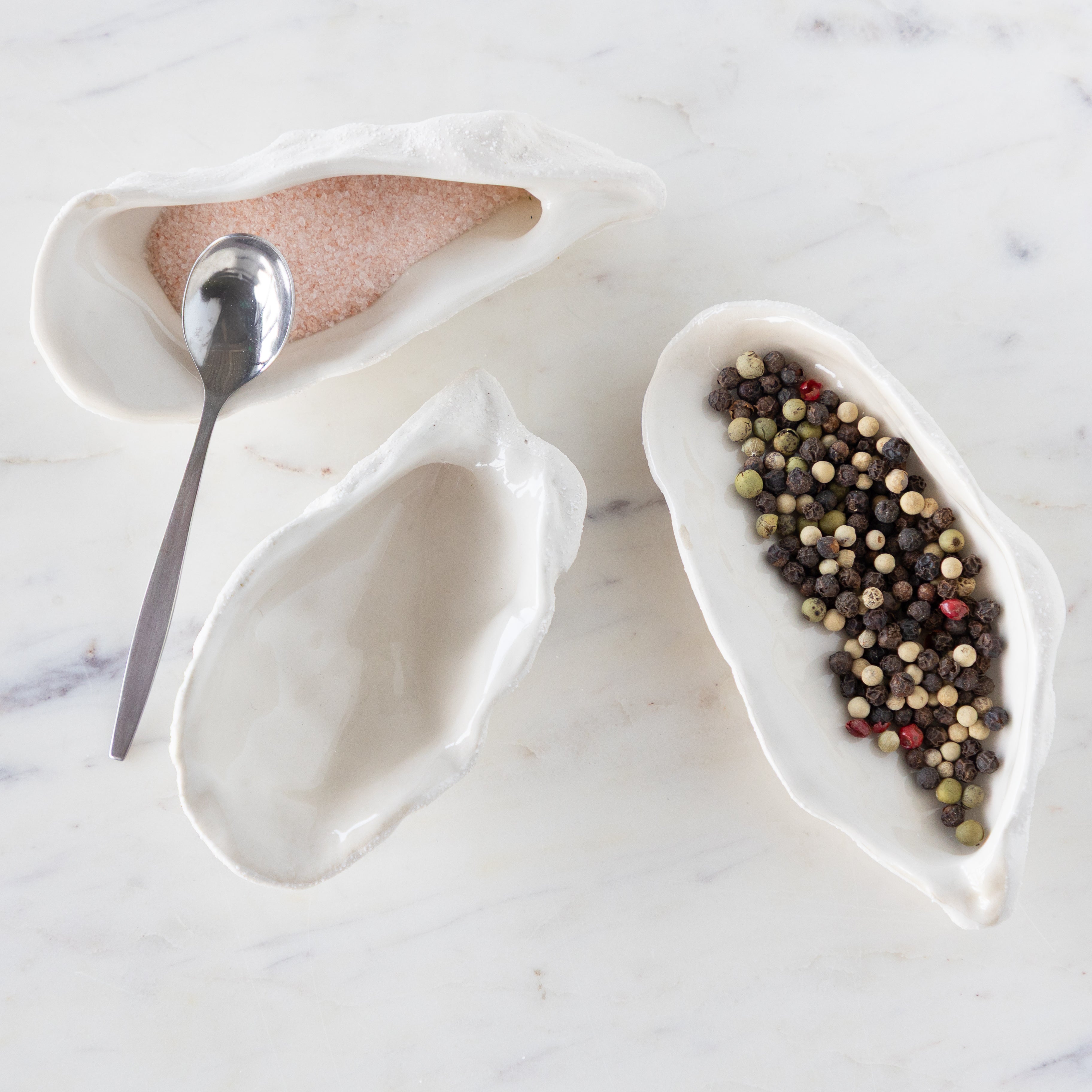 White ceramic oyster-shaped bowls with a spoon on a marble surface.