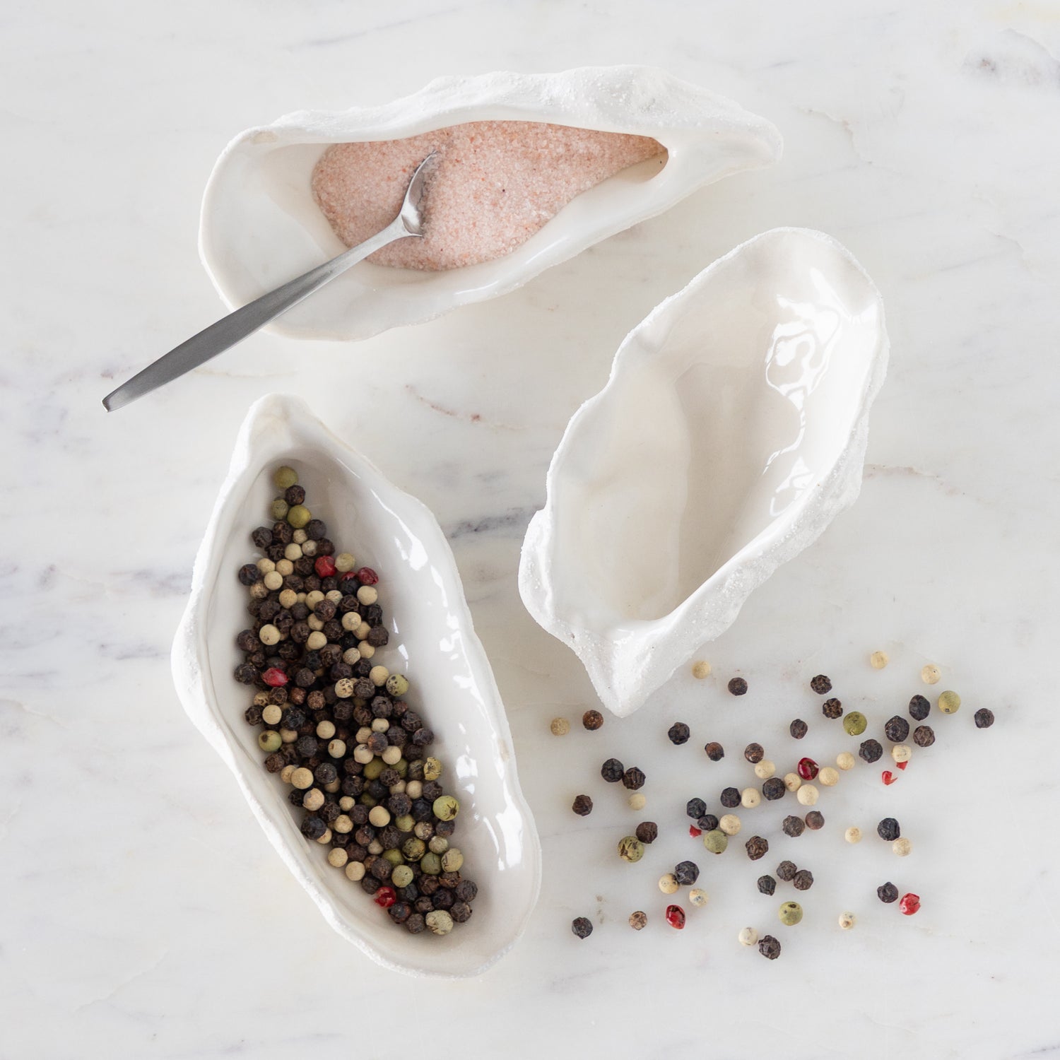 White ceramic oyster-shaped bowls with a spoon on a marble surface.