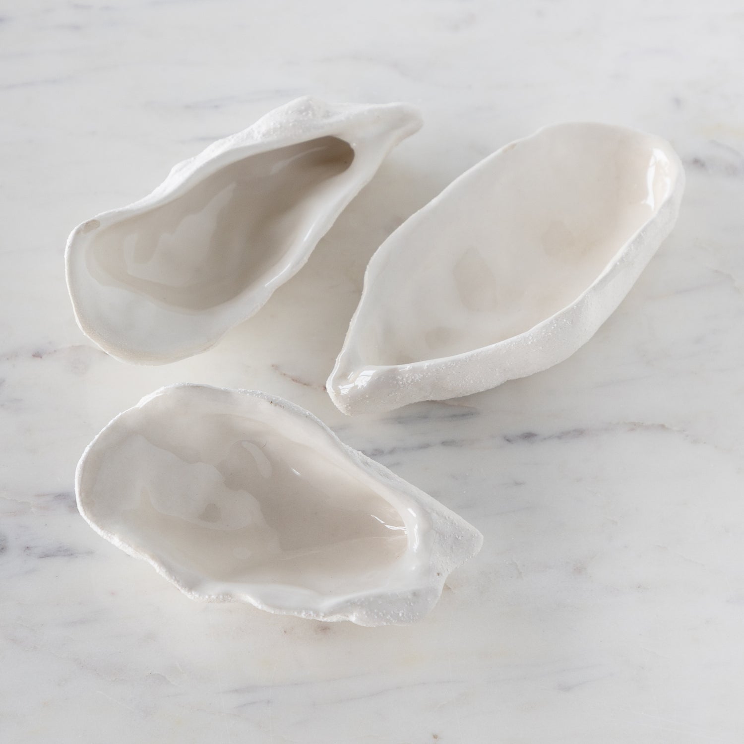 Three white ceramic oyster shells on a marble surface.