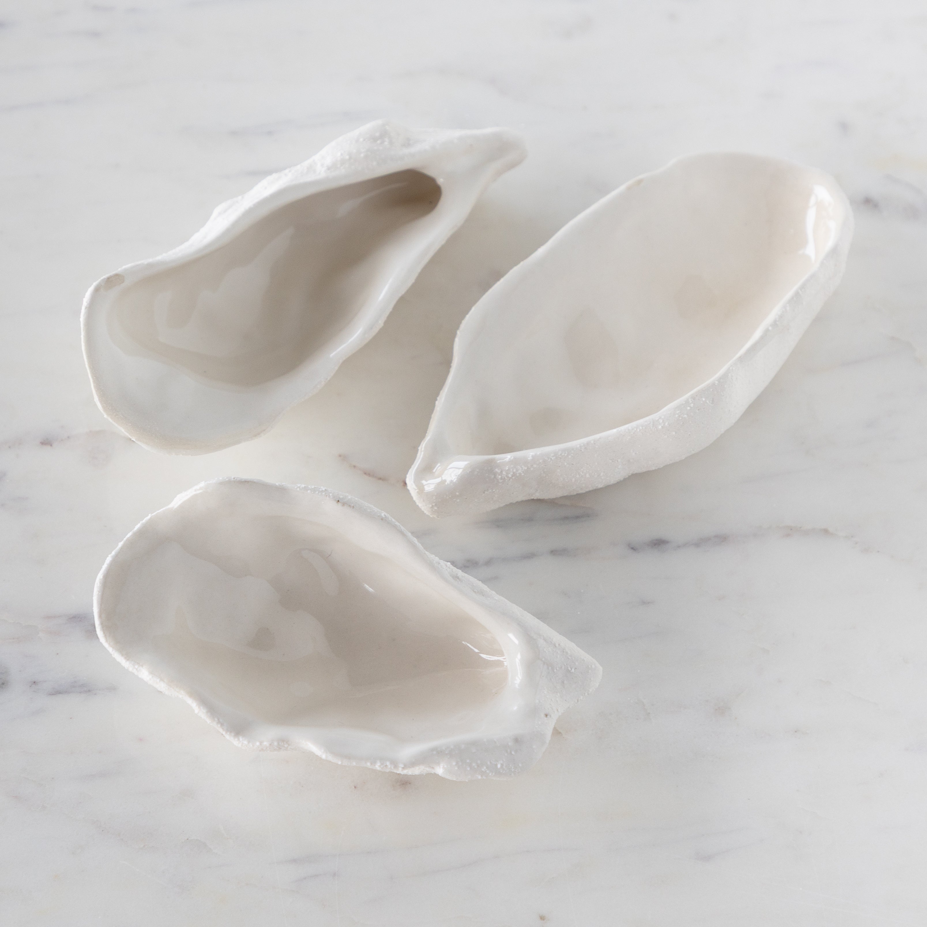 Three white ceramic oyster shells on a marble surface.