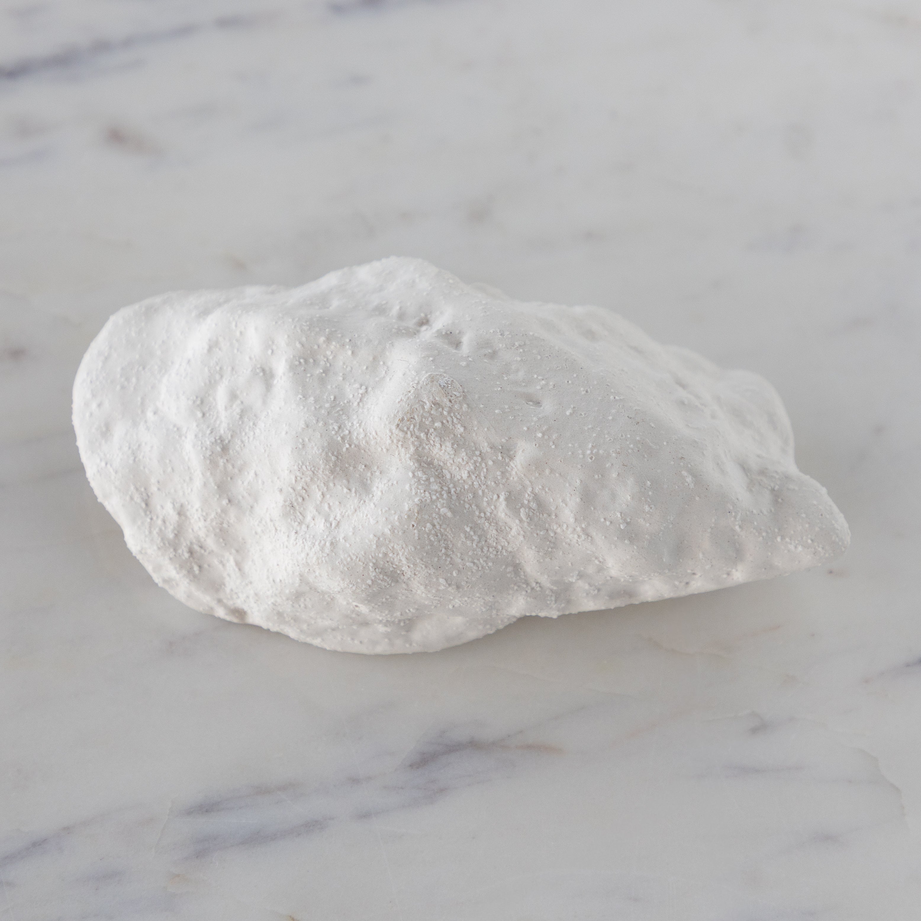 White ceramic oyster-shaped bowl on a marble surface.