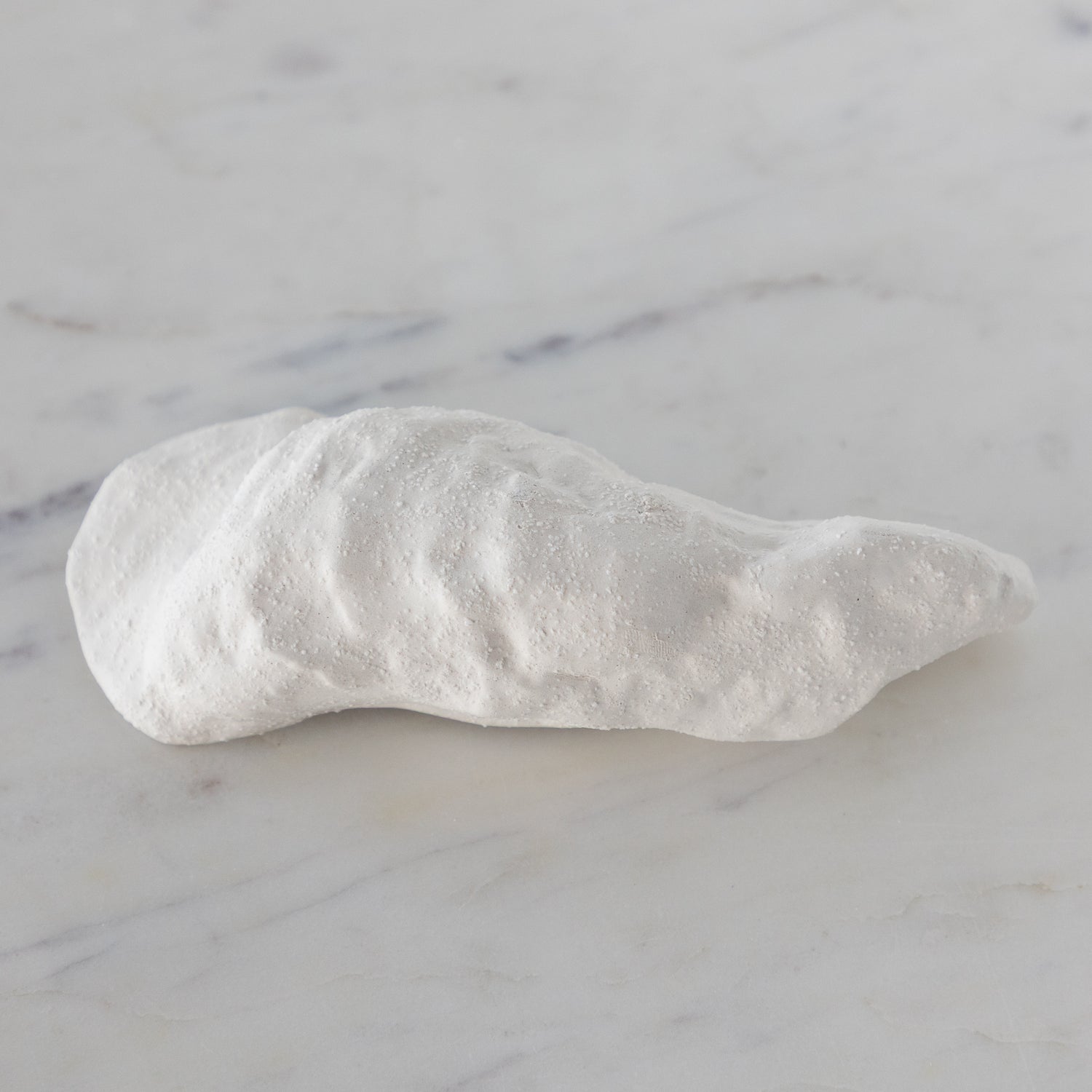 White ceramic oyster-shaped bowl on a marble surface.