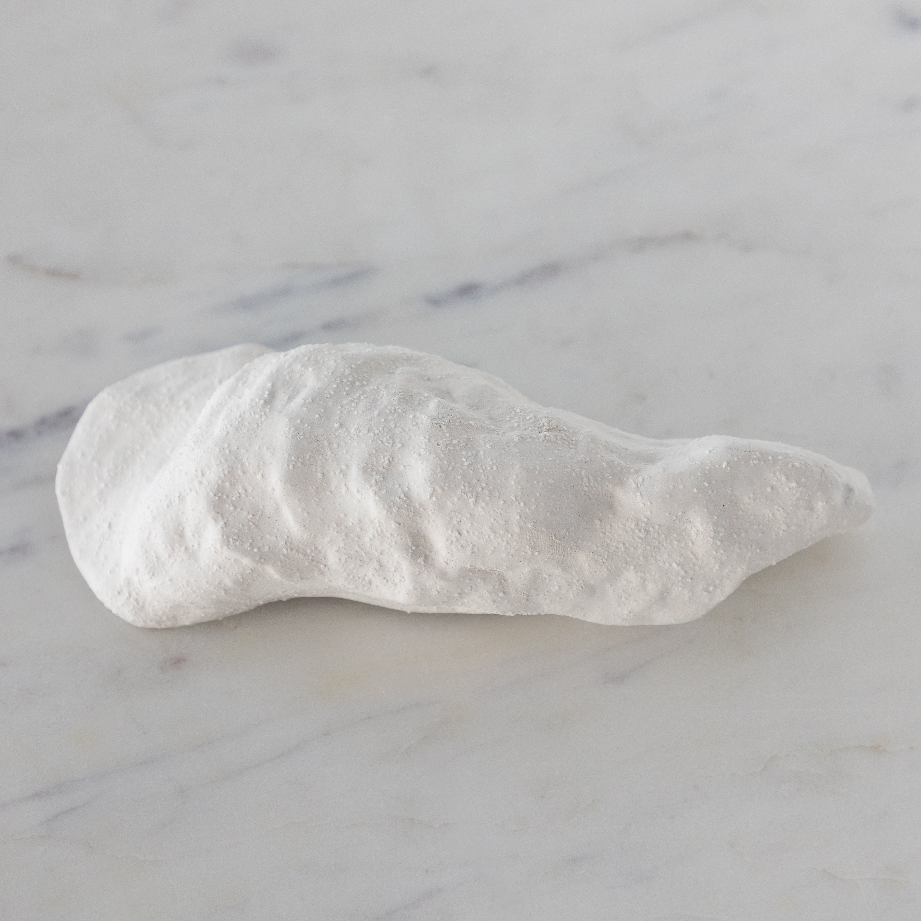 White ceramic oyster-shaped bowl on a marble surface.