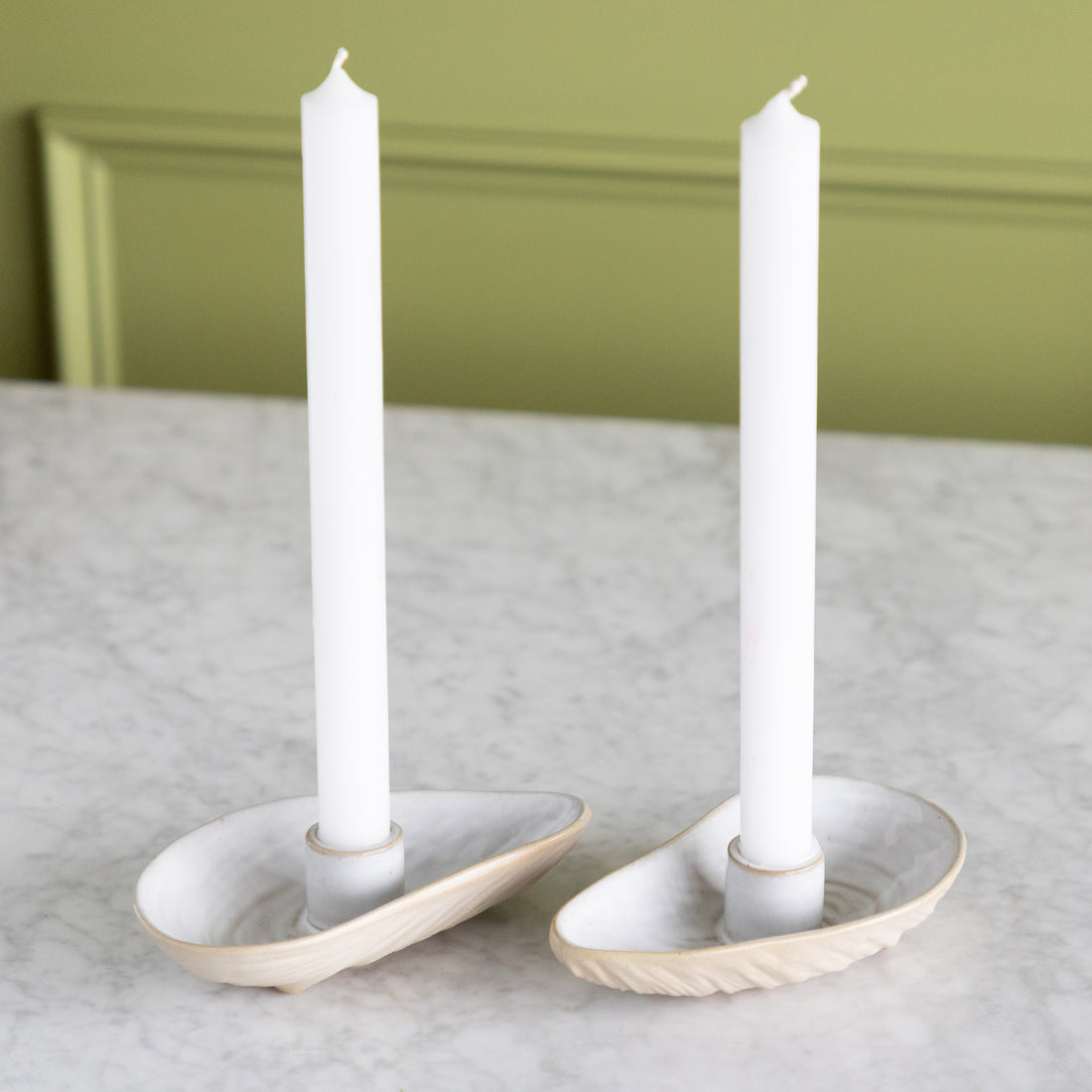 Two oyster shaped candle holders with white taper candles in them. 