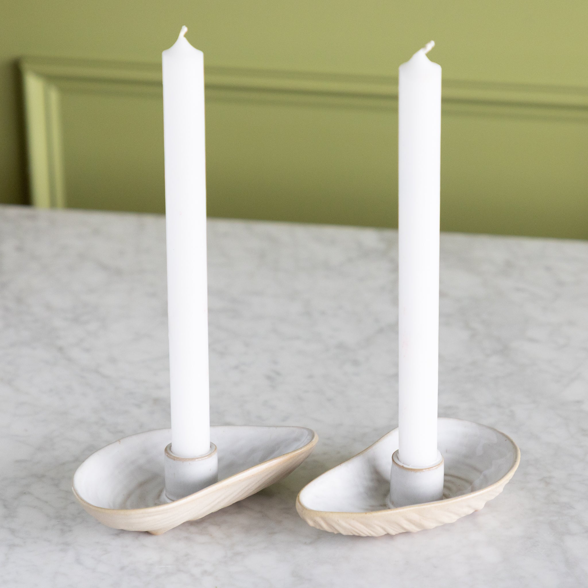 Two oyster shaped candle holders with white taper candles in them. 