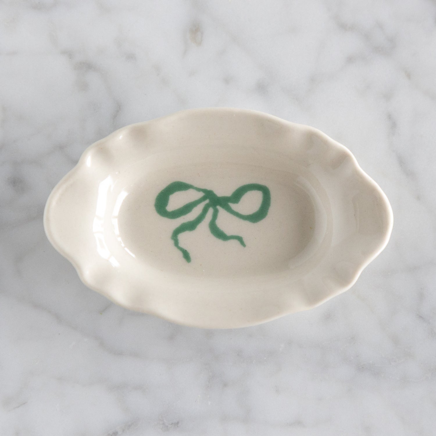 White ceramic dish with a green bow design on a marble surface.