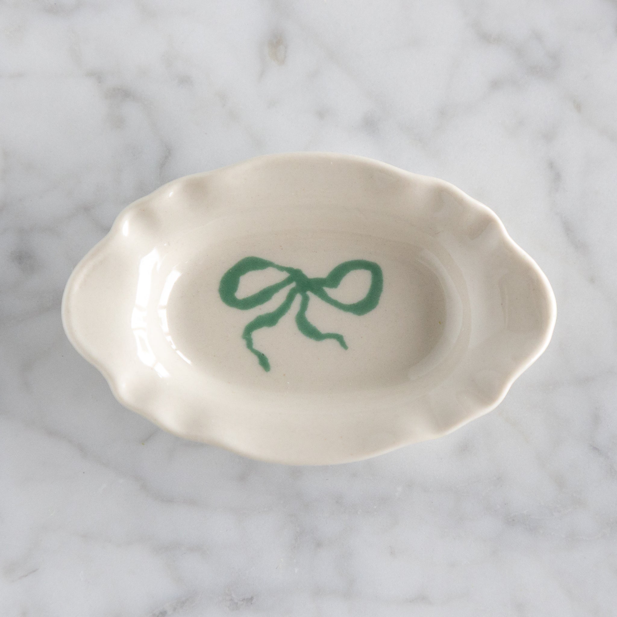 White ceramic dish with a green bow design on a marble surface.