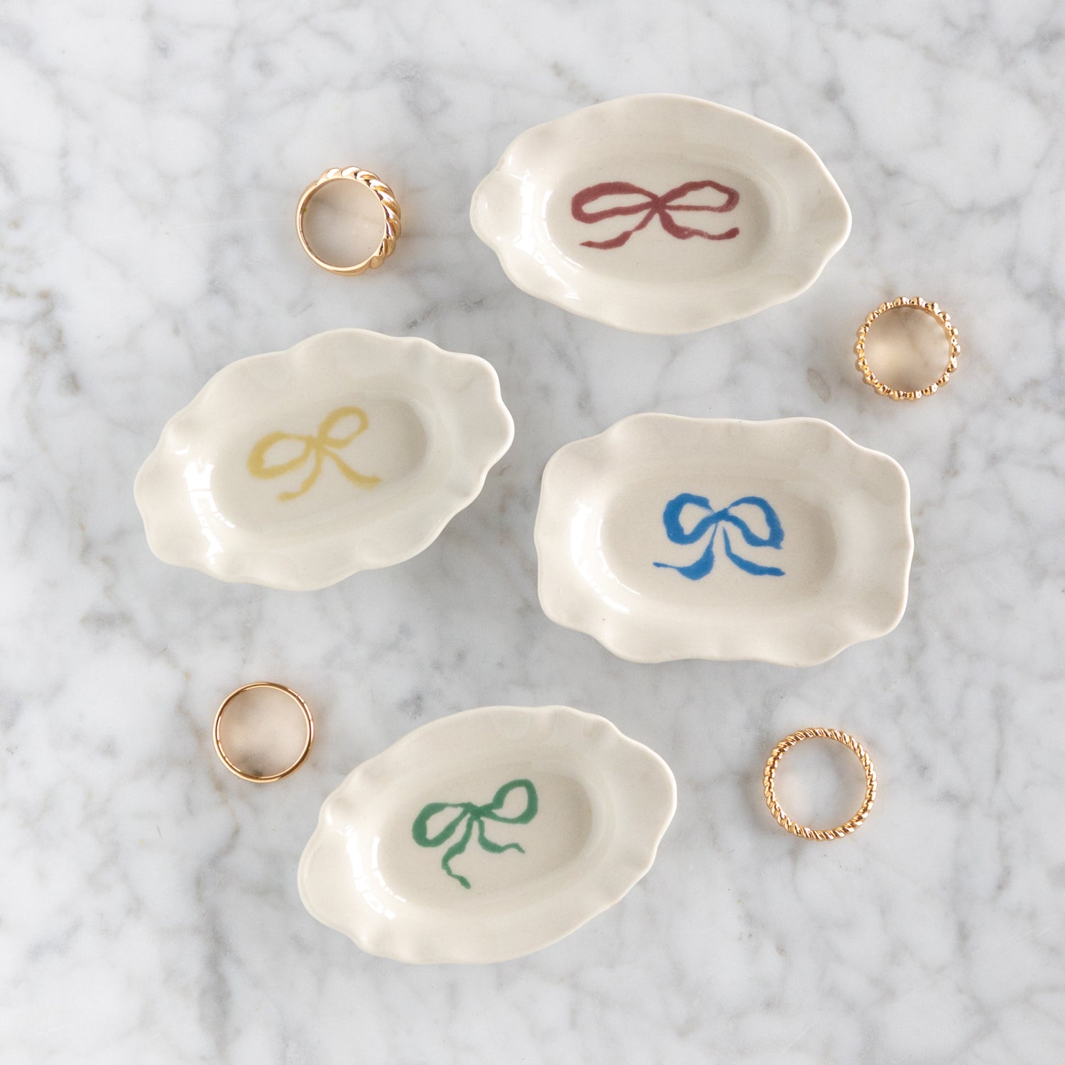 Set of four small ceramic dishes with colorful bow designs on a marble surface with rings.