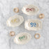 Set of four small ceramic dishes with colorful bow designs on a marble surface with rings.