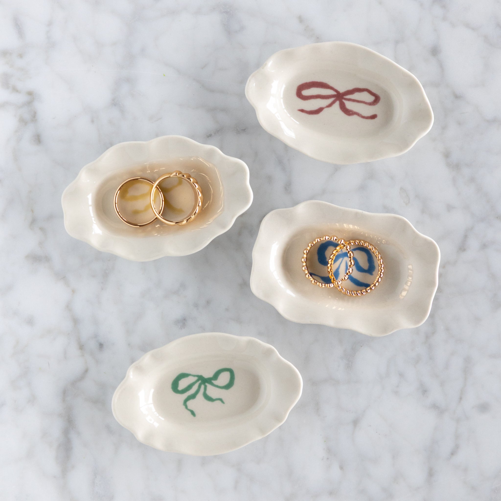 Set of four small white ceramic dishes with decorative bows on a marble surface –– two with gold rings in them.