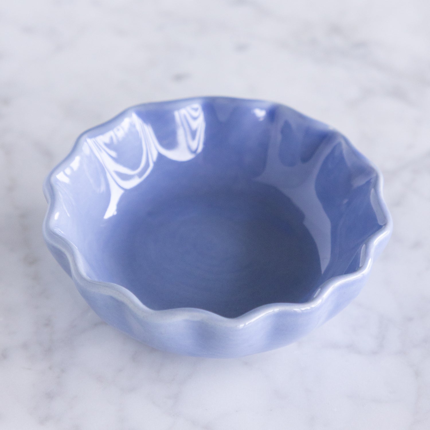 Blue ceramic dish with a scalloped edge on a marble table.