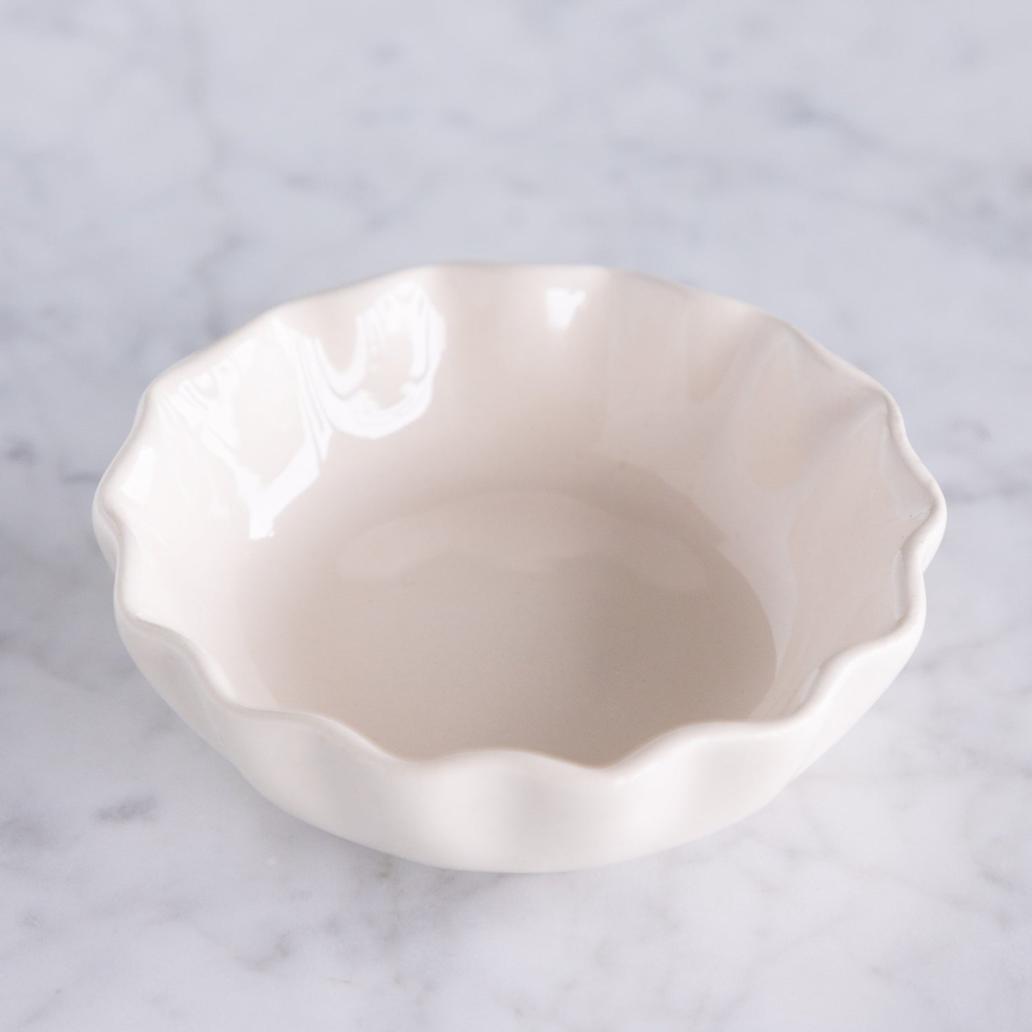 White ceramic dish with a scalloped edge on a marble table.