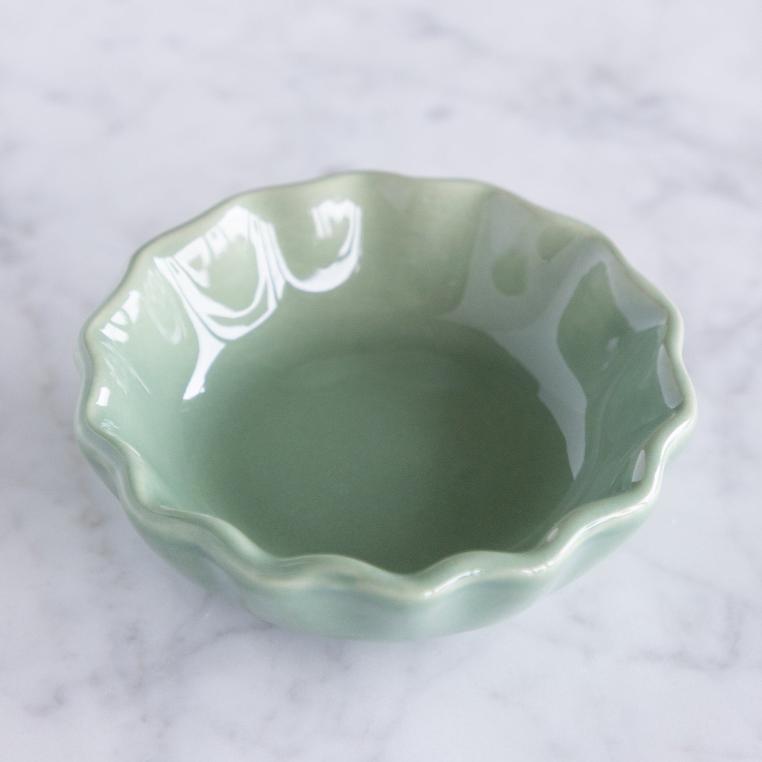 Green ceramic dish with a scalloped edge on a marble table.