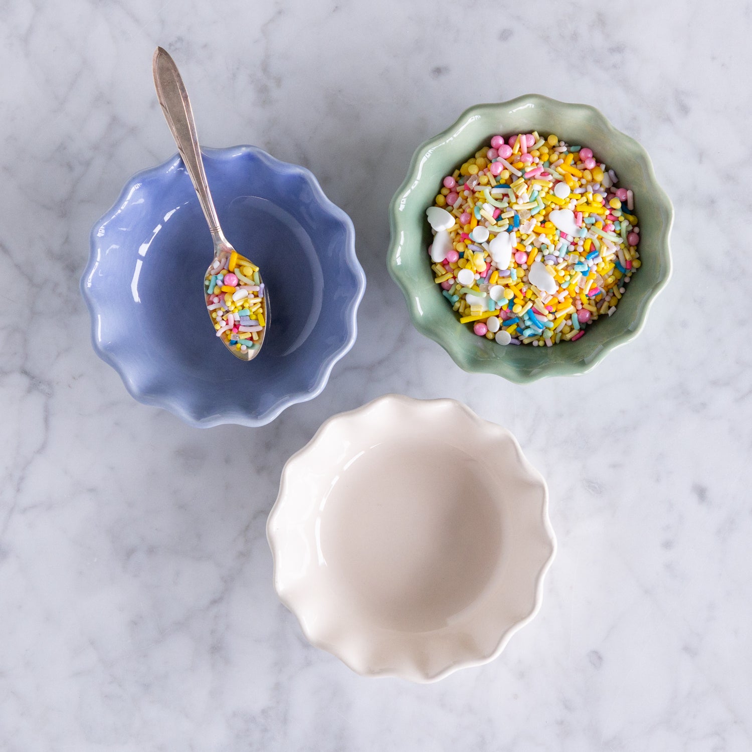 Three ceramic bowls in green, white and cream with colorful sprinkles on a marble surface.