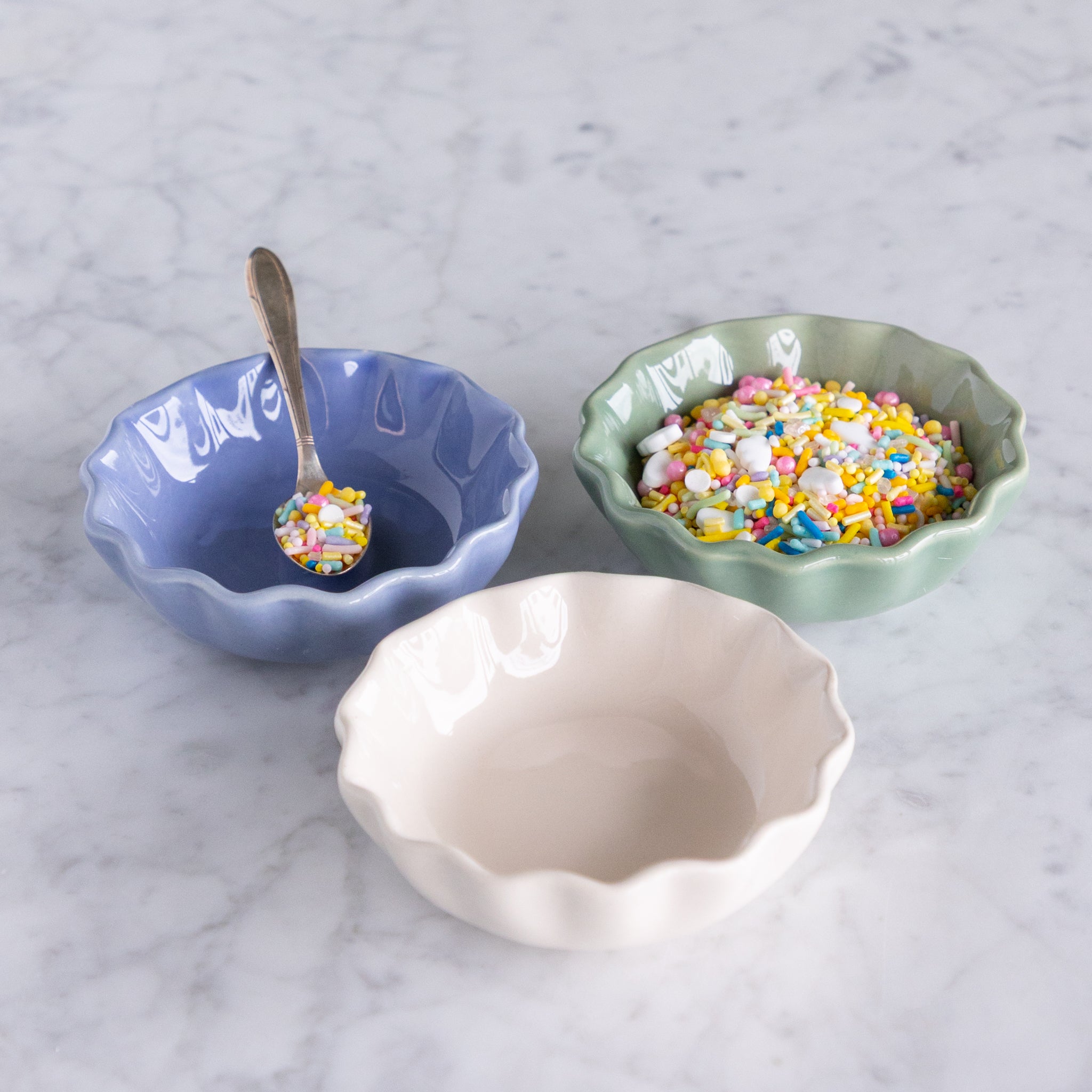 Three ceramic bowls in green, white and cream with colorful sprinkles on a marble surface.