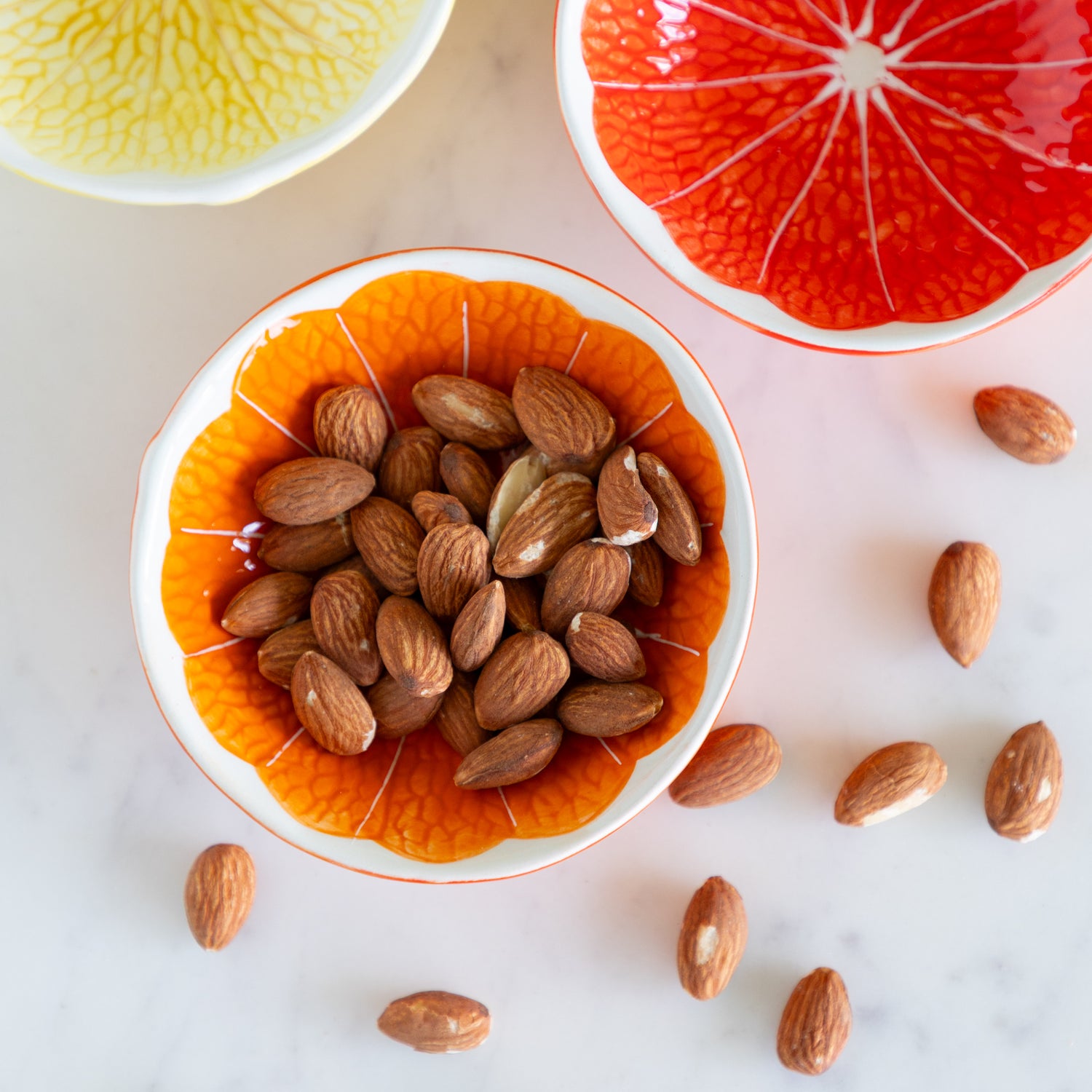 Almonds in an orange Ceramic Citrus Fruit Shaped Bowl on a marble table.