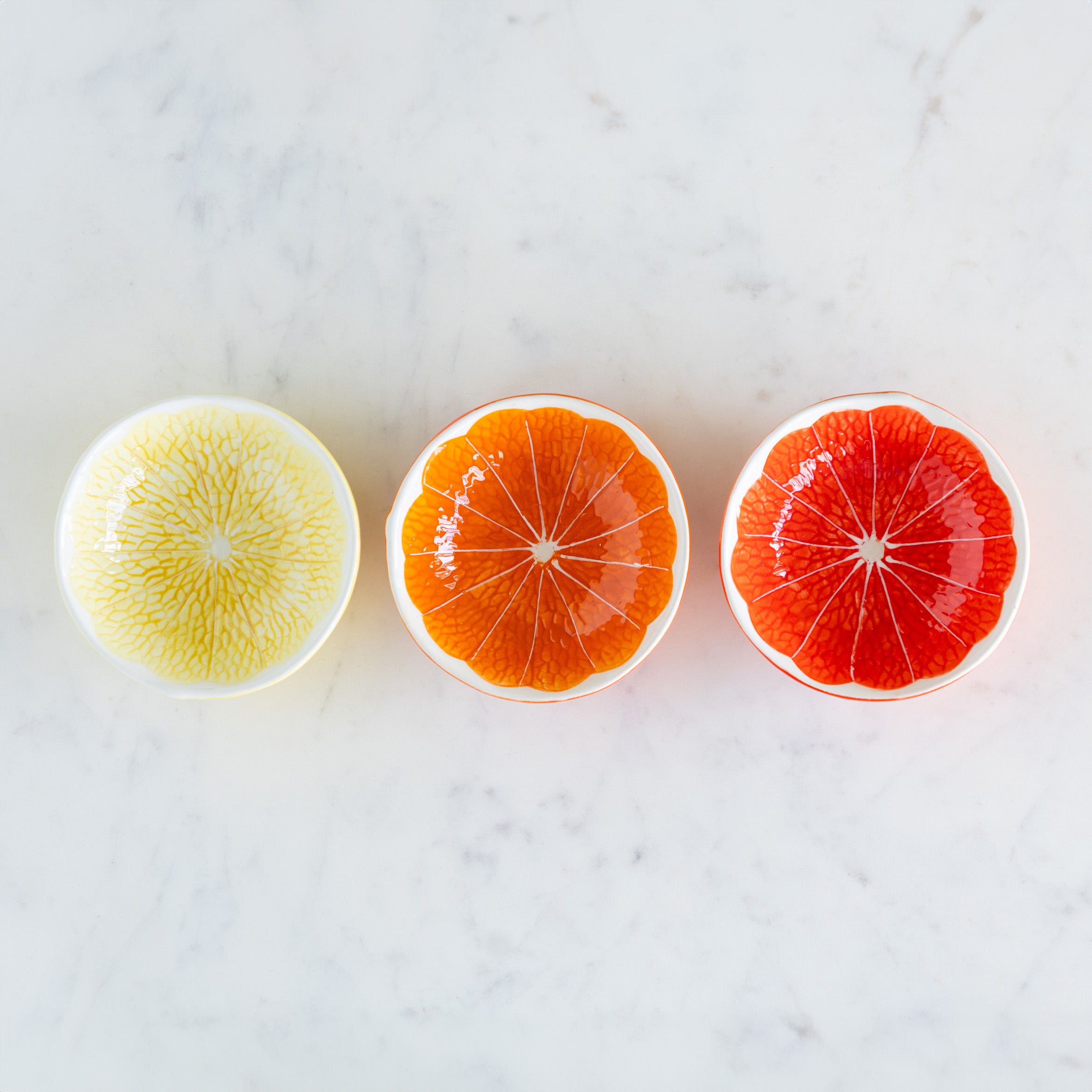 Three Ceramic Citrus Fruit Shaped Bowls on a marble table.
