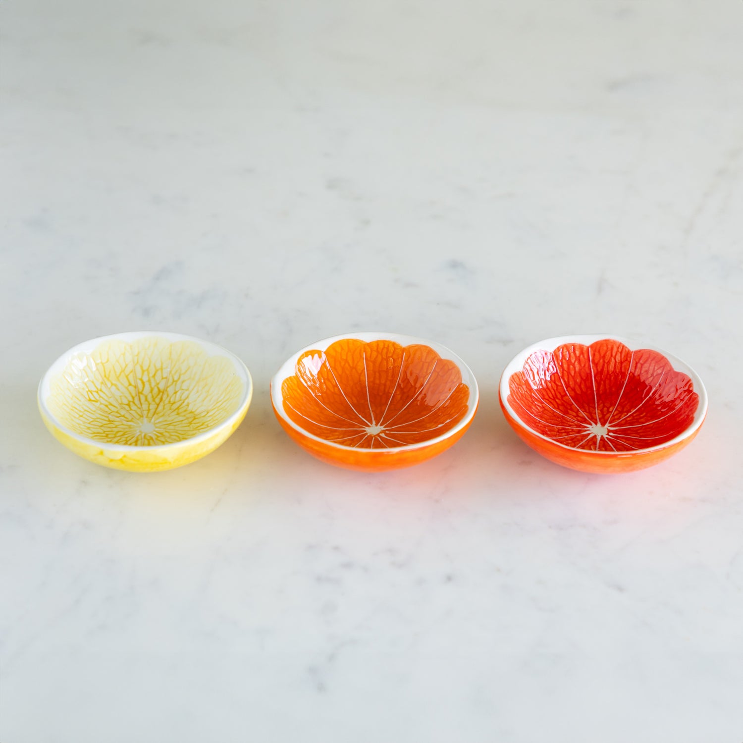 Three Ceramic Citrus Fruit Shaped Bowls on a marble table.