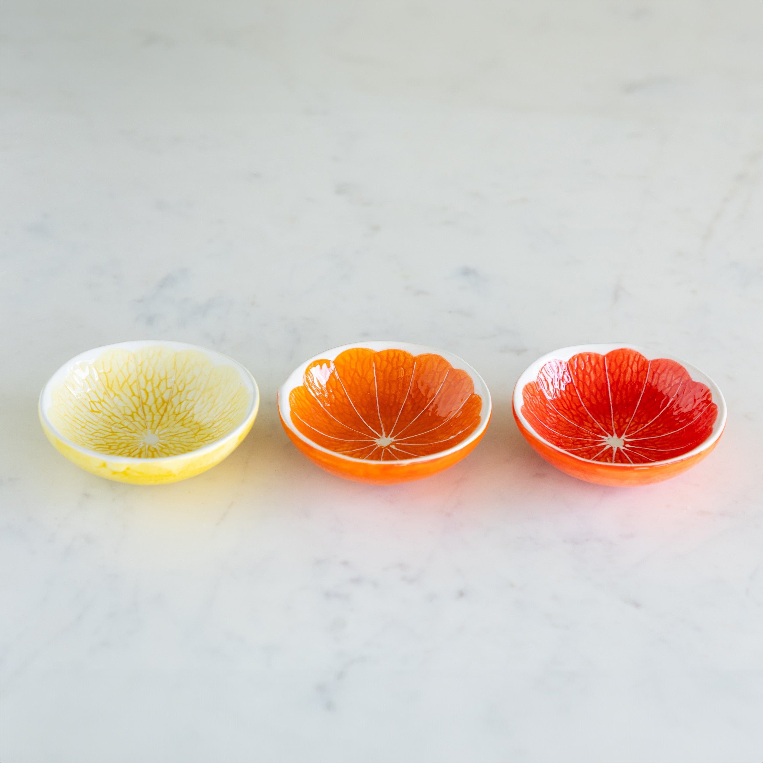 Three Ceramic Citrus Fruit Shaped Bowls on a marble table.