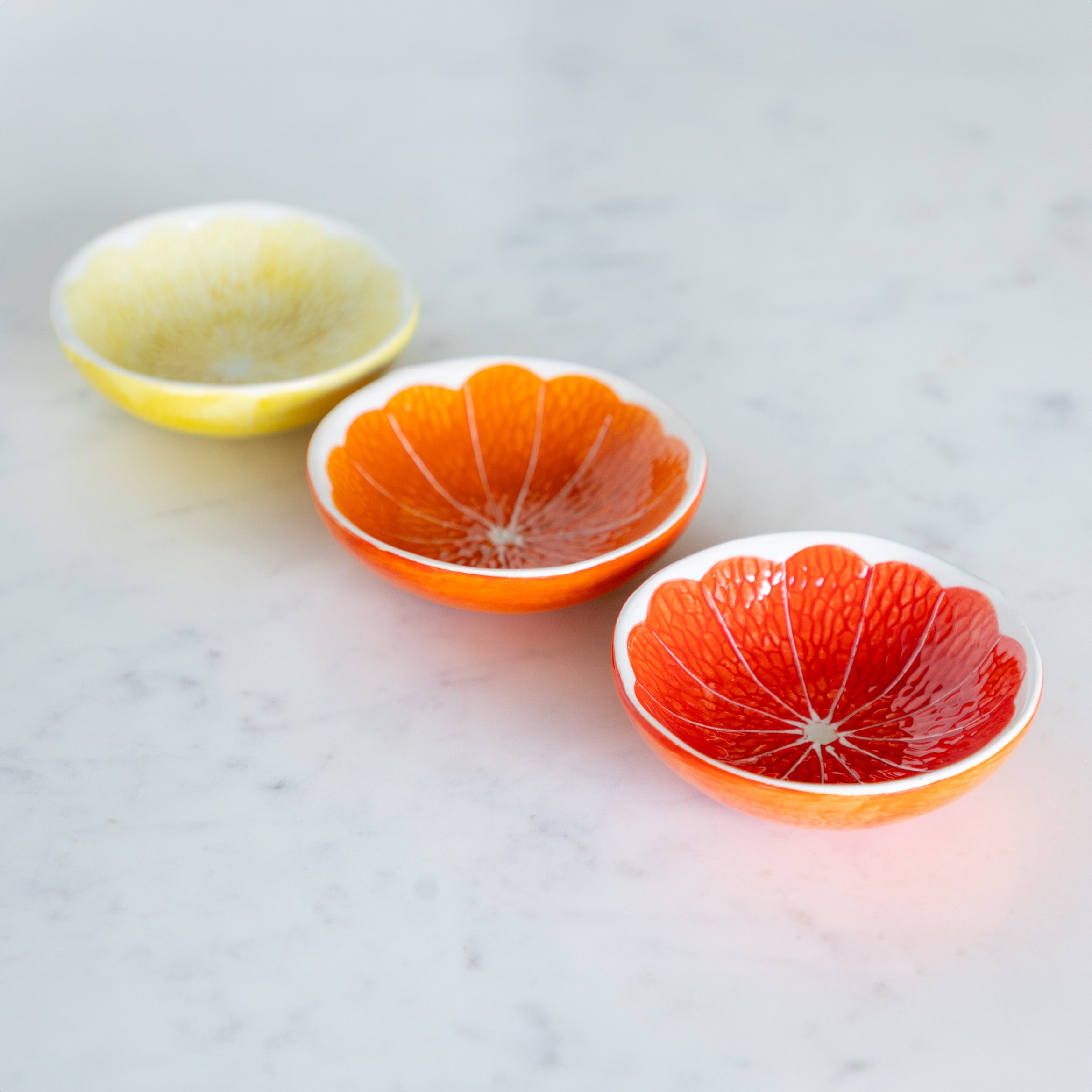 Three Ceramic Citrus Fruit Shaped Bowls on a marble table.