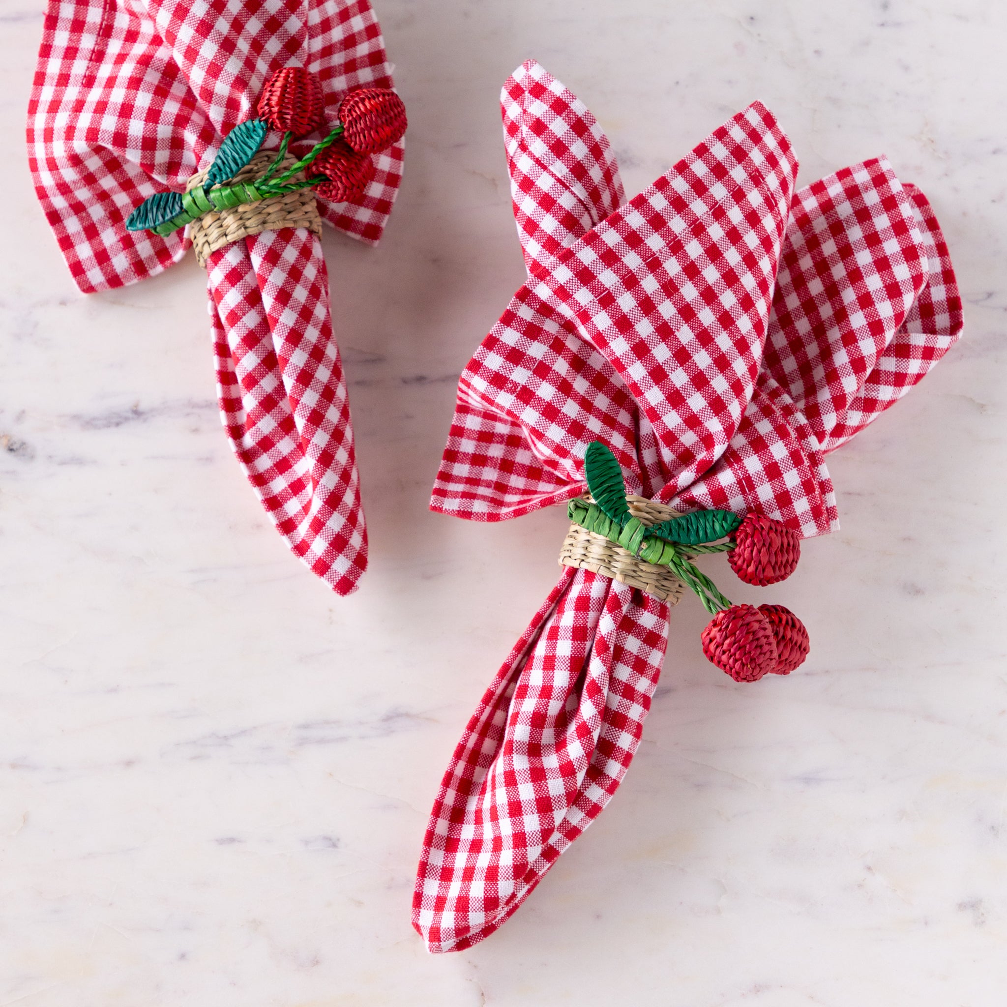 Red and white checkered napkins with woven seagrass cherry napkin rings on a marble surface.