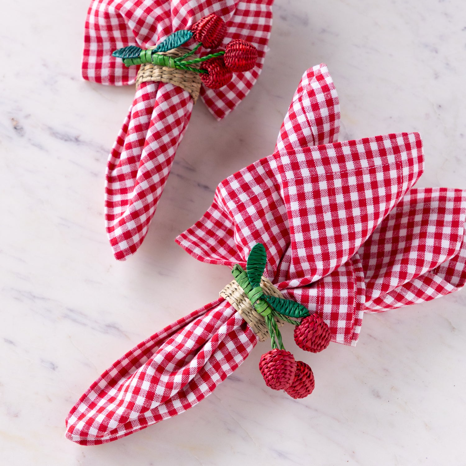 Red and white checkered napkins with woven seagrass cherry napkin rings on a marble surface.