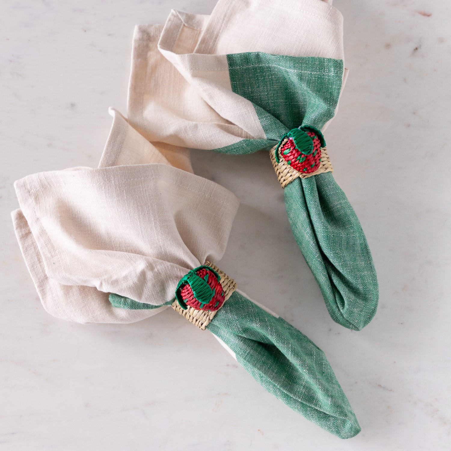 Green napkins with strawberry-themed napkin rings on a white surface.