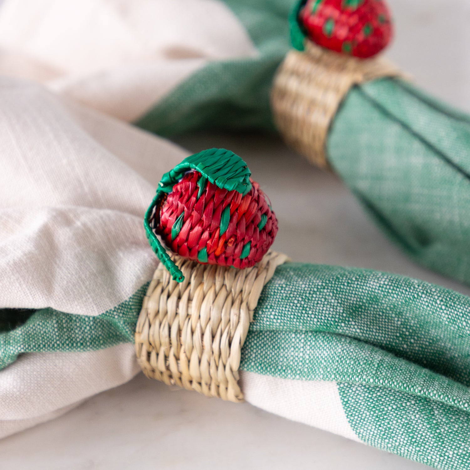 Green napkins with strawberry-themed napkin rings on a white surface.