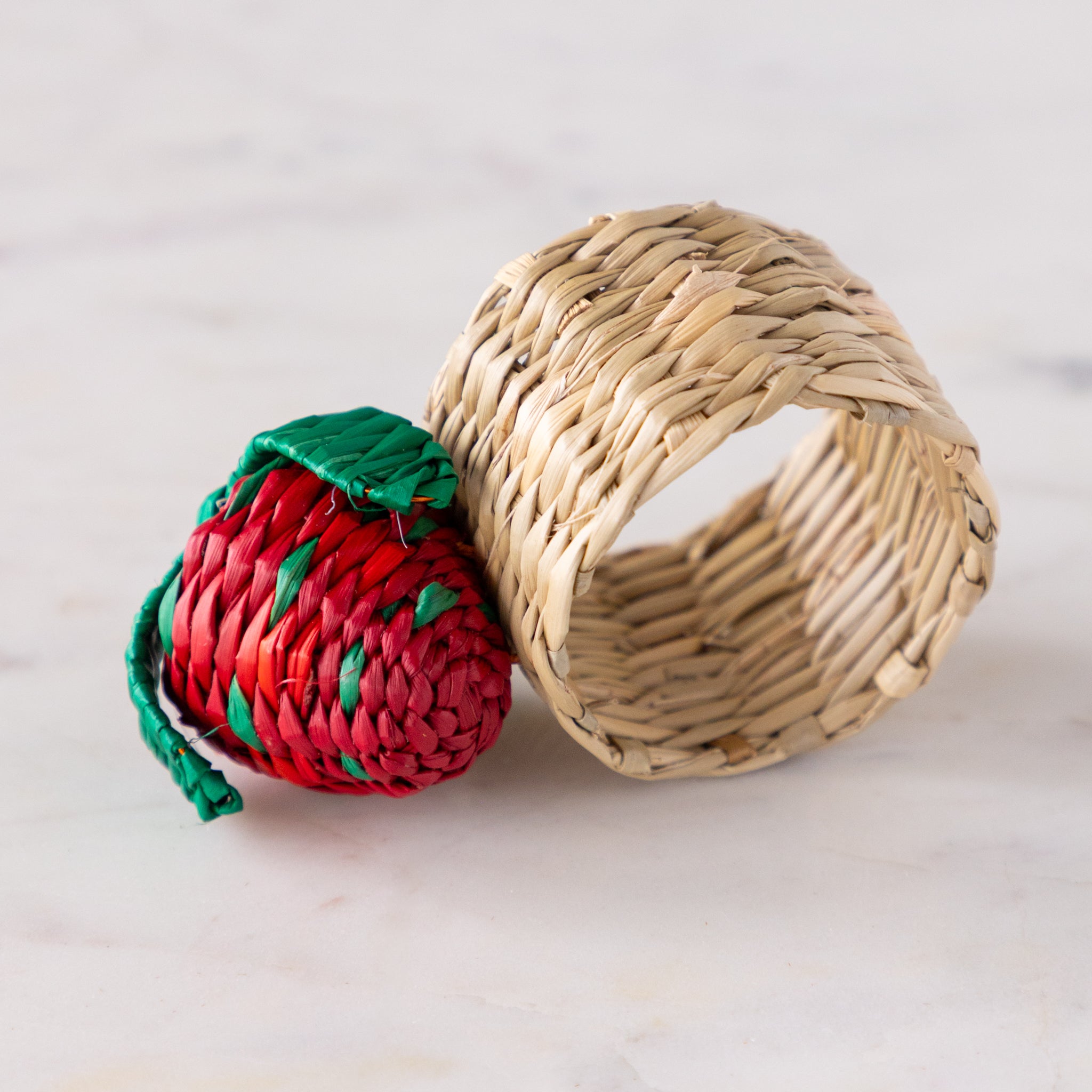 Woven seagrass napkin ring with a strawberry design on a marble table.