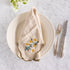 Beige embroidered daisies napkin on a white plate with silverware on a marble surface.