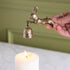 Hand holding a gold hare-shaped candle snuffer with a bell over a lit candle against a green background.