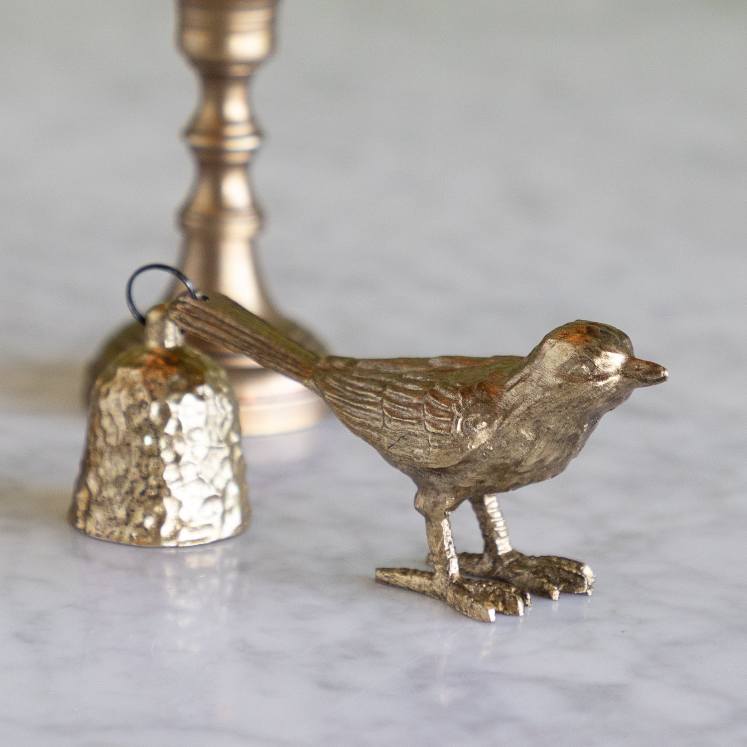 Bronze bird-shaped bell candle snuffer on a marble surface with a blurred green background.