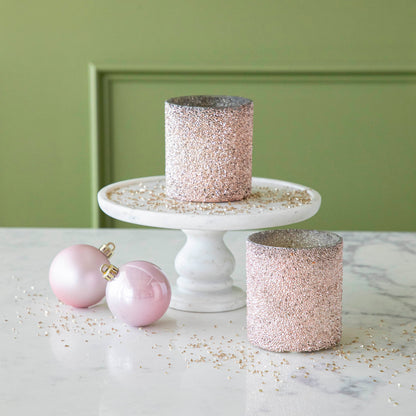 Pink Shimmer Votives styled with one on a cake stand and one on the table, surrounded by glitter and two pink ornaments.